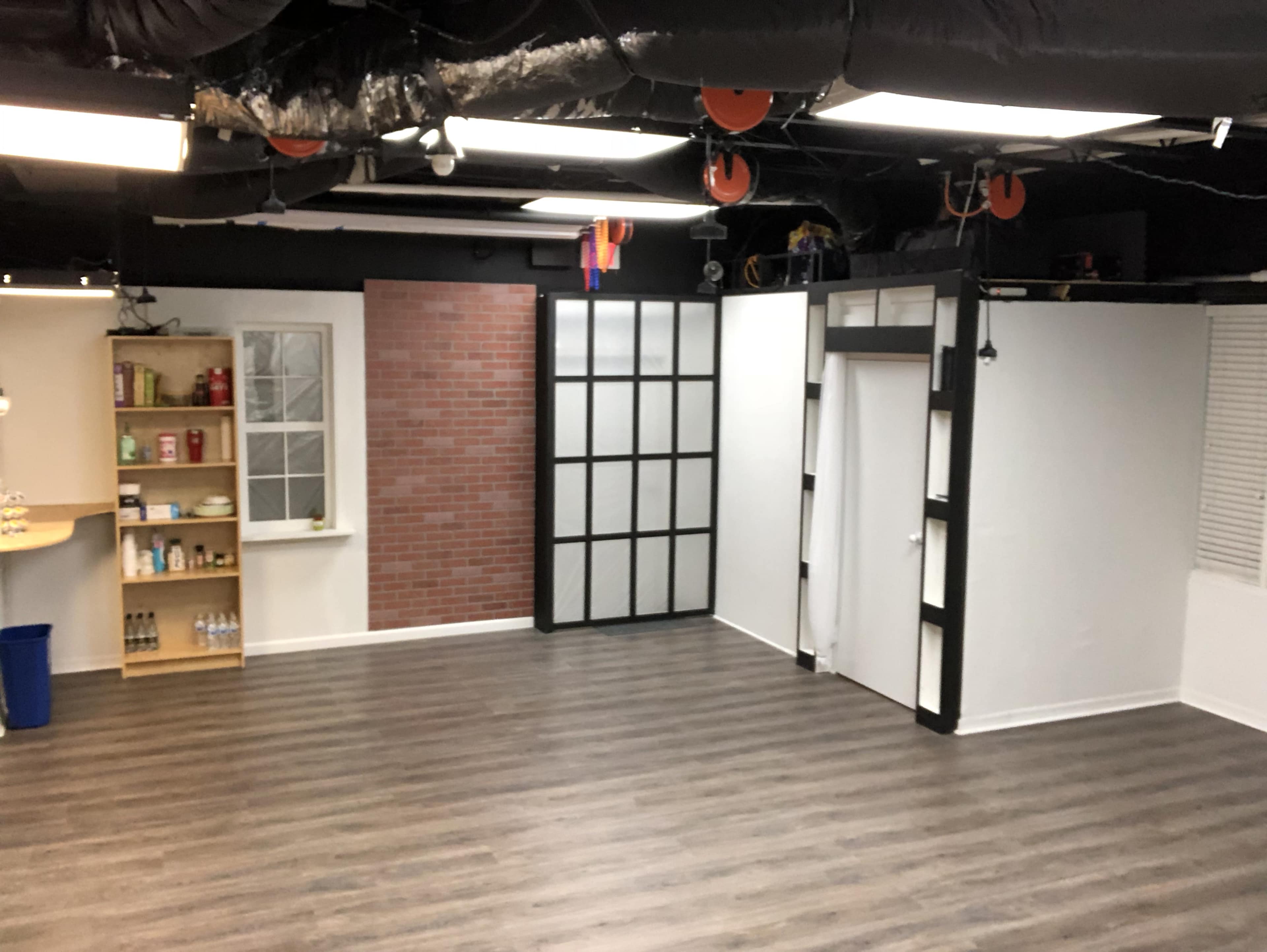 An empty room with hardwood floors, a bookshelf against one wall, and partitions creating a couple of distinct sections.