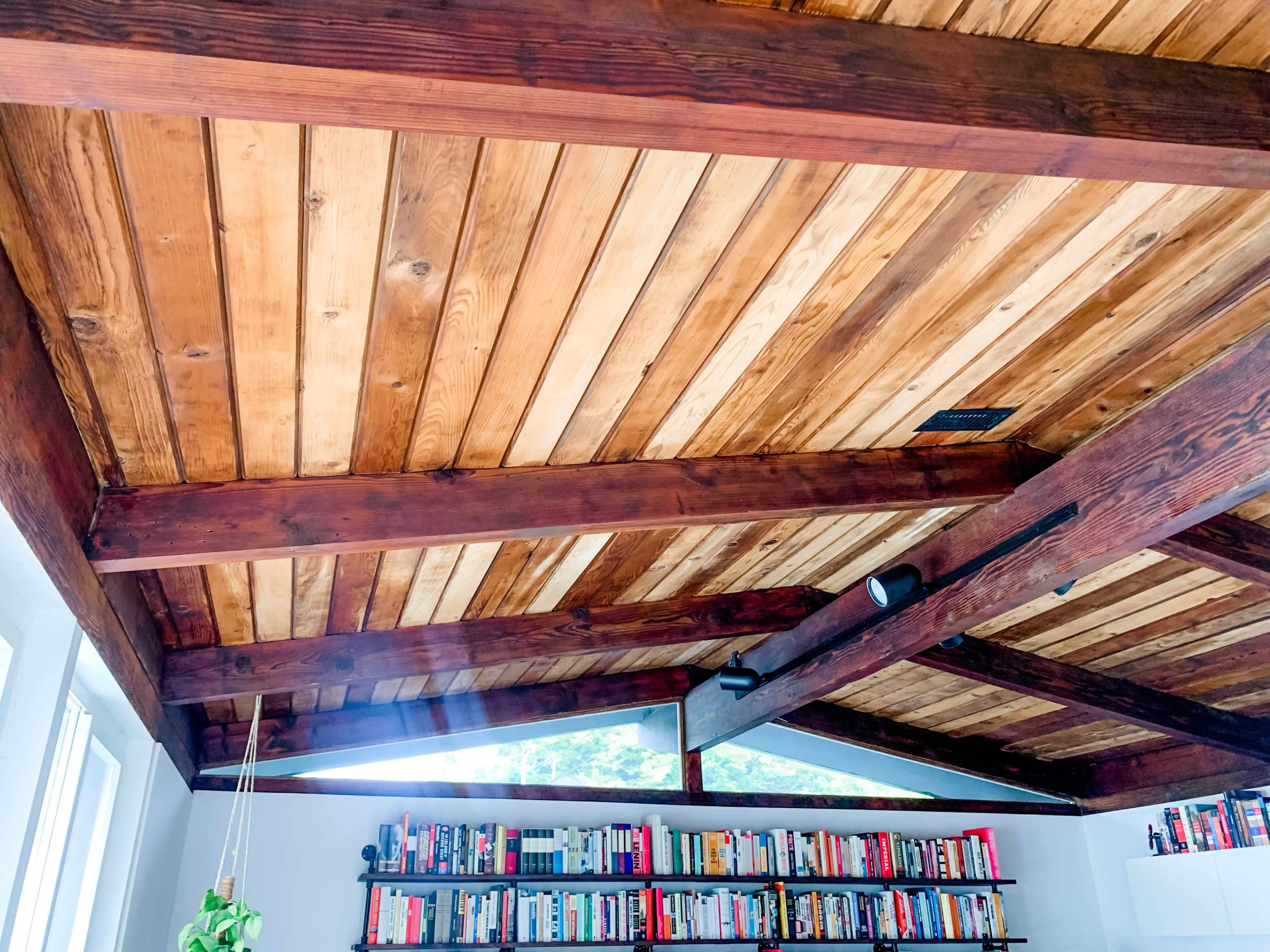 A wooden ceiling with exposed beams above a bookshelf filled with books in a well-lit room.