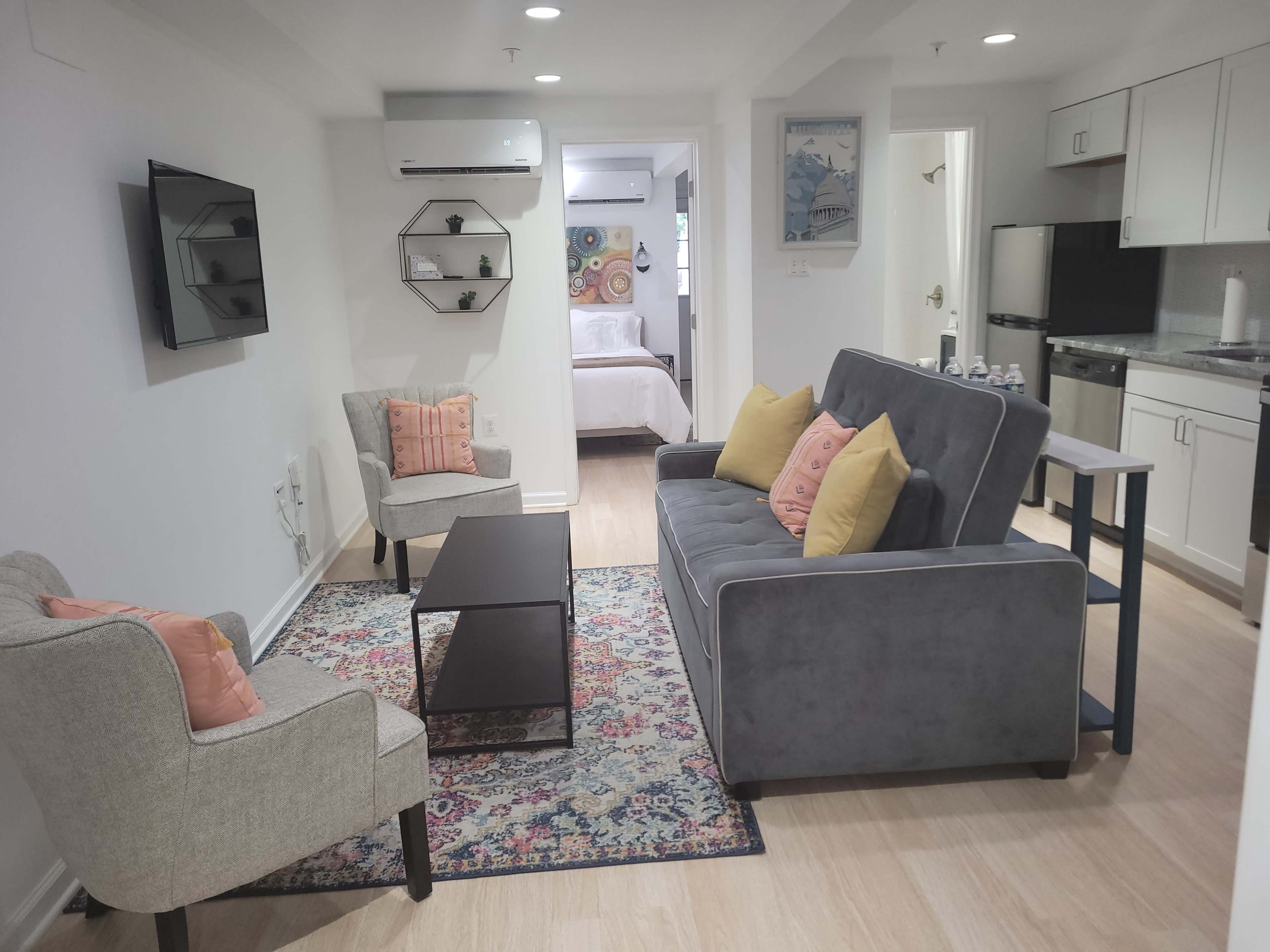 A modern living space with a gray sofa, two light-colored chairs, a coffee table, and a wall-mounted television, all arranged around a patterned rug.
