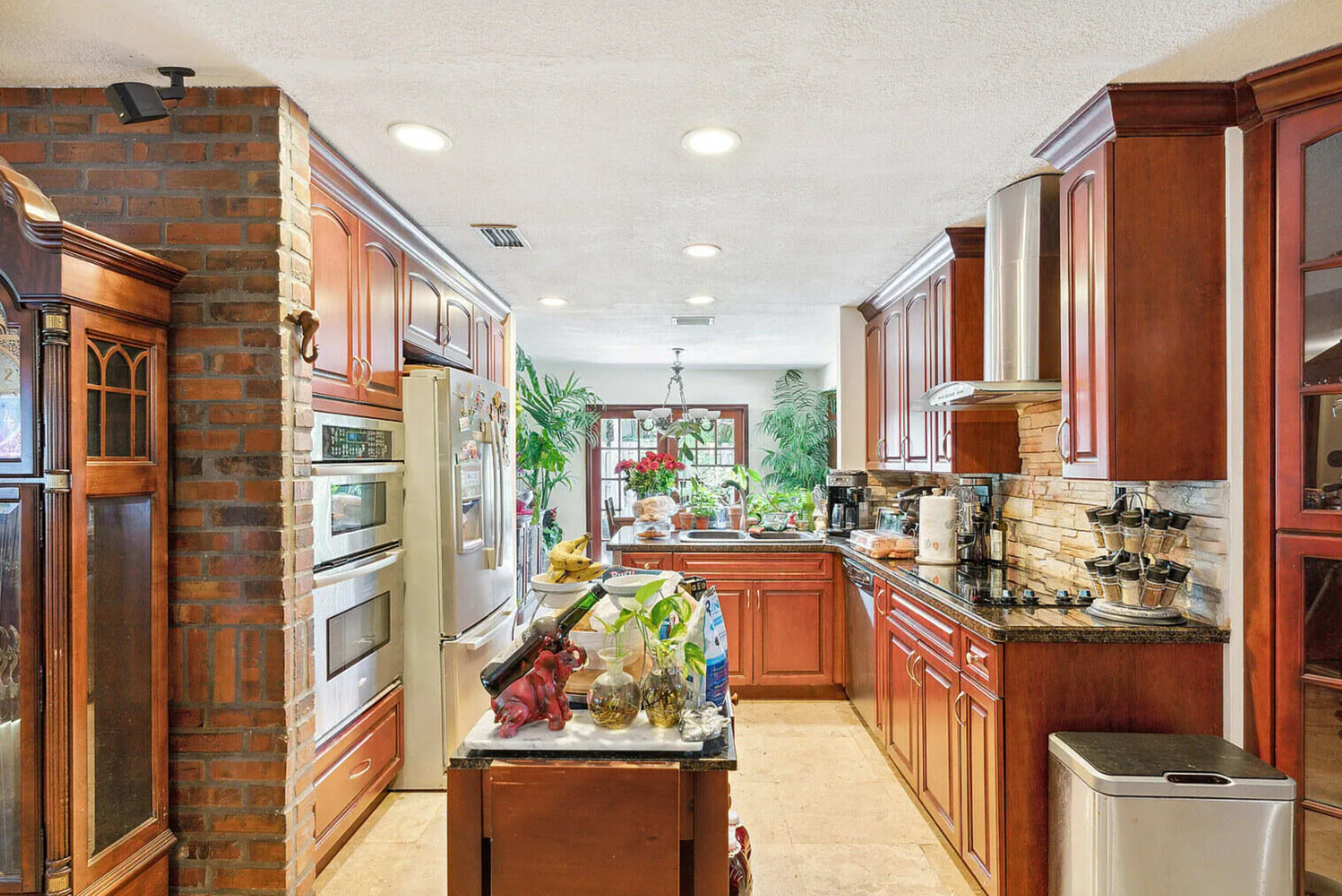 The kitchen features wooden cabinetry, stainless steel appliances, and a stone backsplash, along with a view of indoor plants.