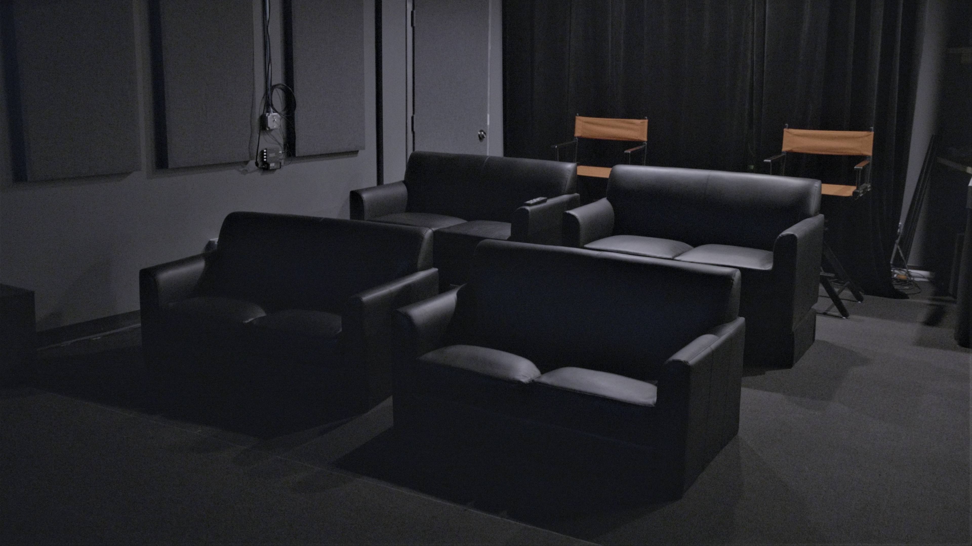 Several black leather sofas arranged in a dimly lit room with a couple of director's chairs in the background.