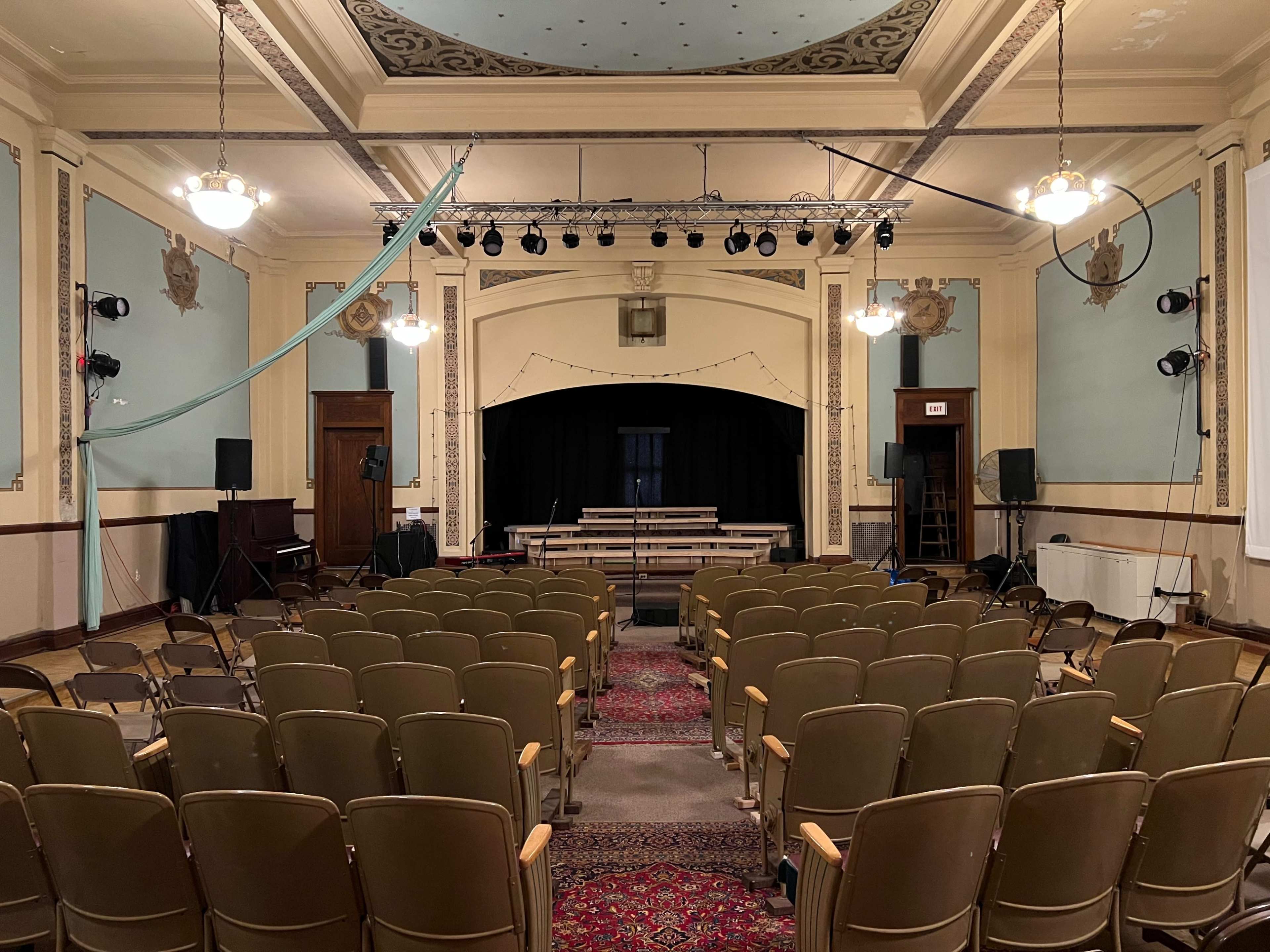 A theater interior with rows of empty seats facing a stage equipped with curtains and lighting fixtures.