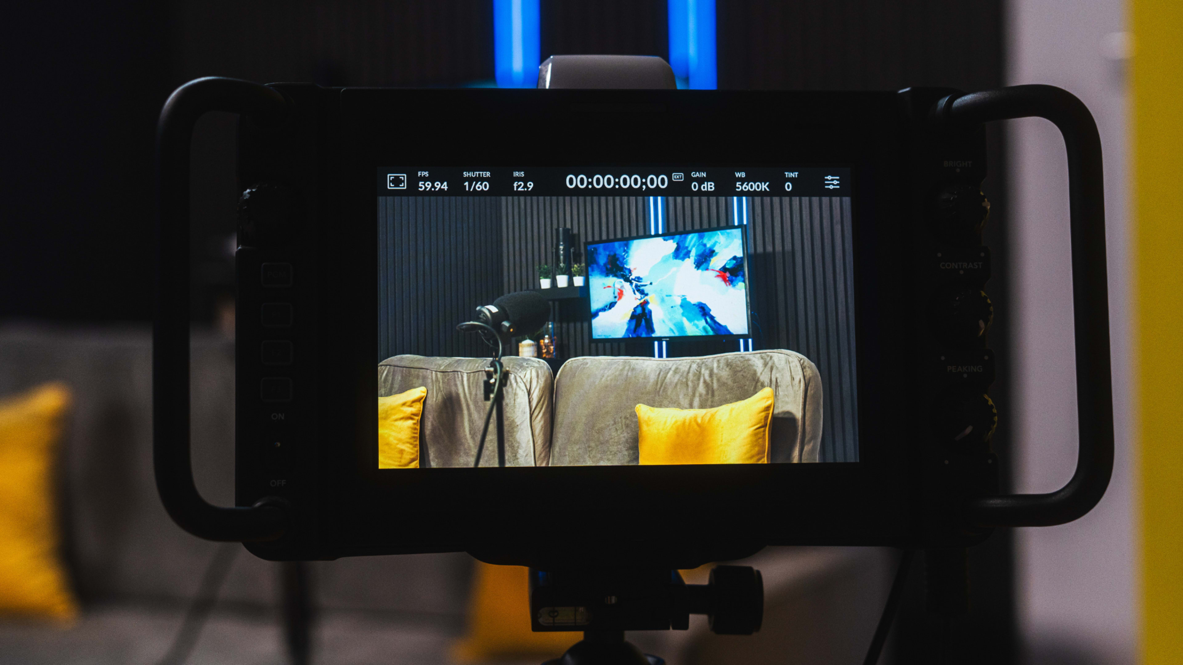 A camera monitor displays a scene of a couch with cushions in a studio setup.