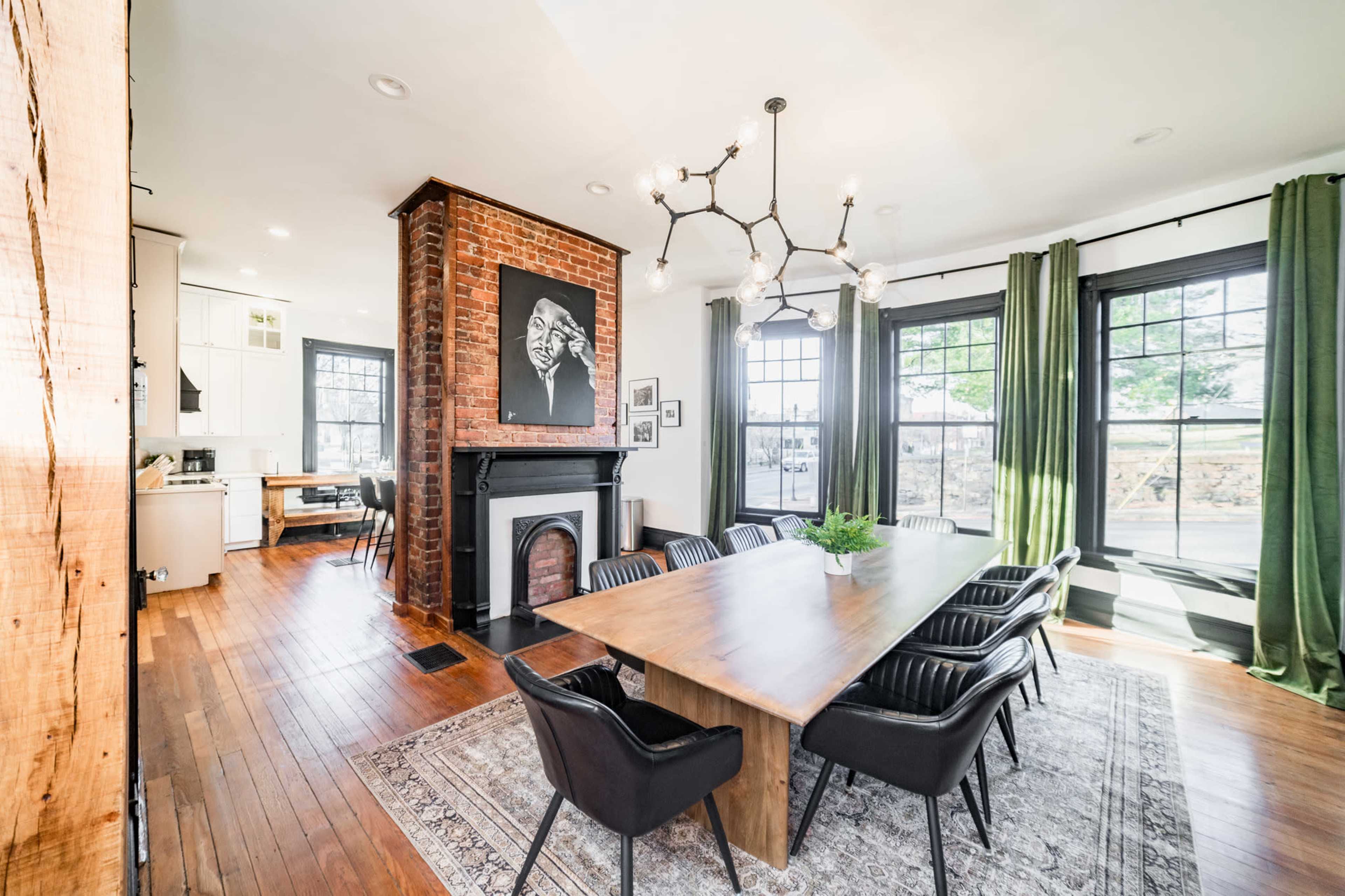 A spacious dining area featuring a large wooden table surrounded by black chairs, with a fireplace and large windows allowing natural light.