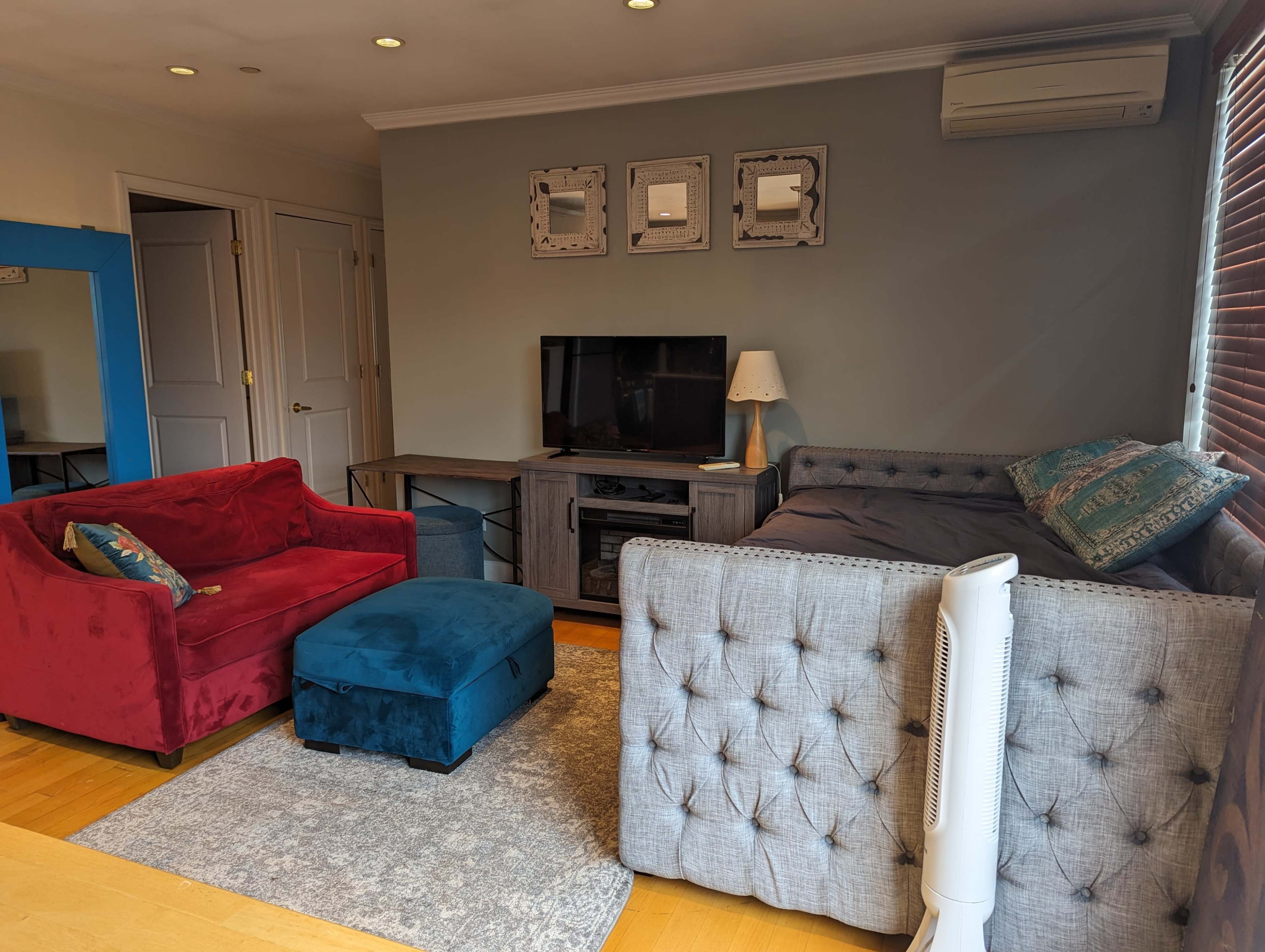 The living room features a red loveseat, a gray sectional sofa, a black television on a wooden stand, and a blue ottoman on a light rug.
