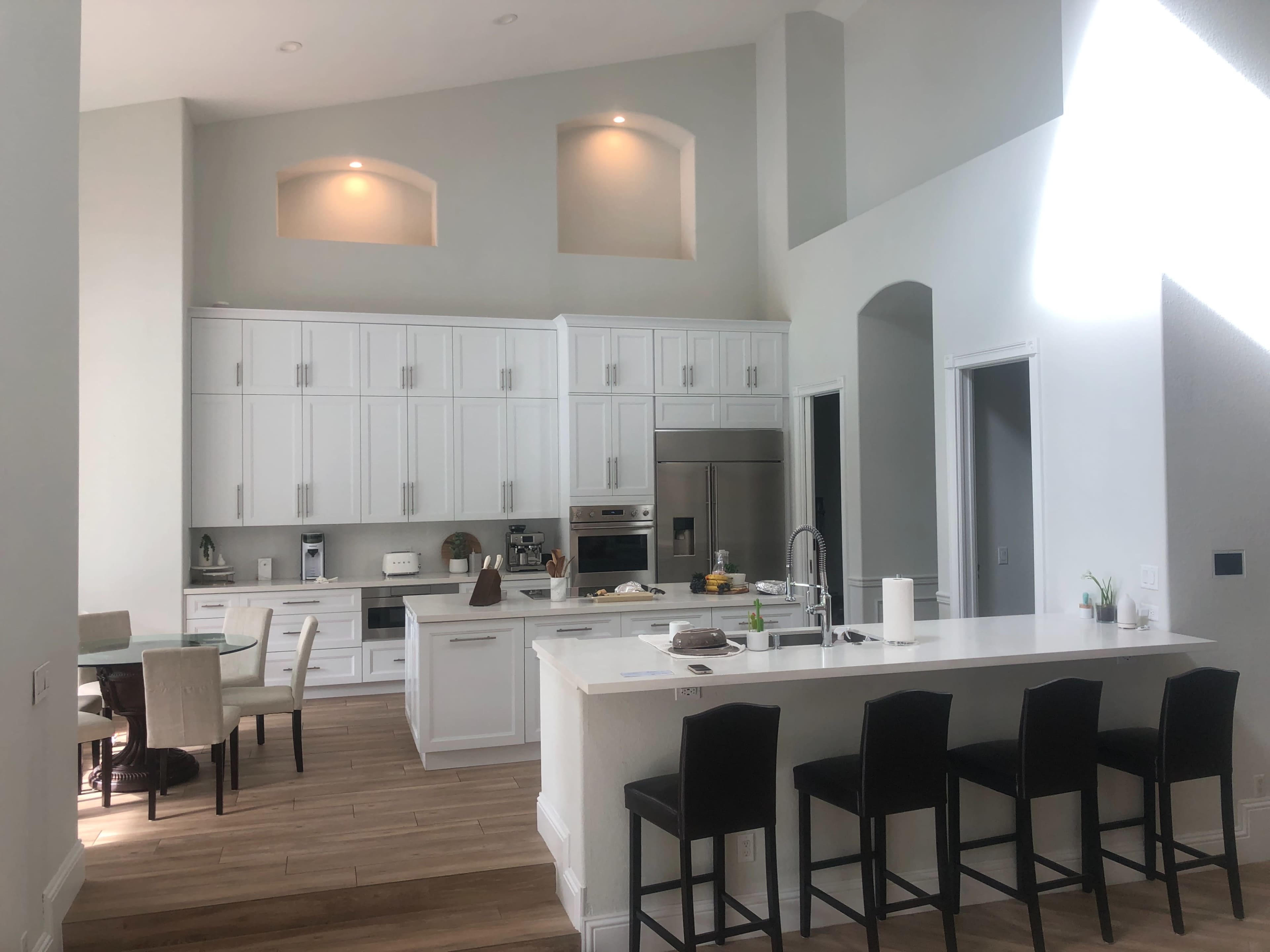 A modern kitchen with white cabinetry, a central island with seating, and a dining area featuring a round table and chairs.