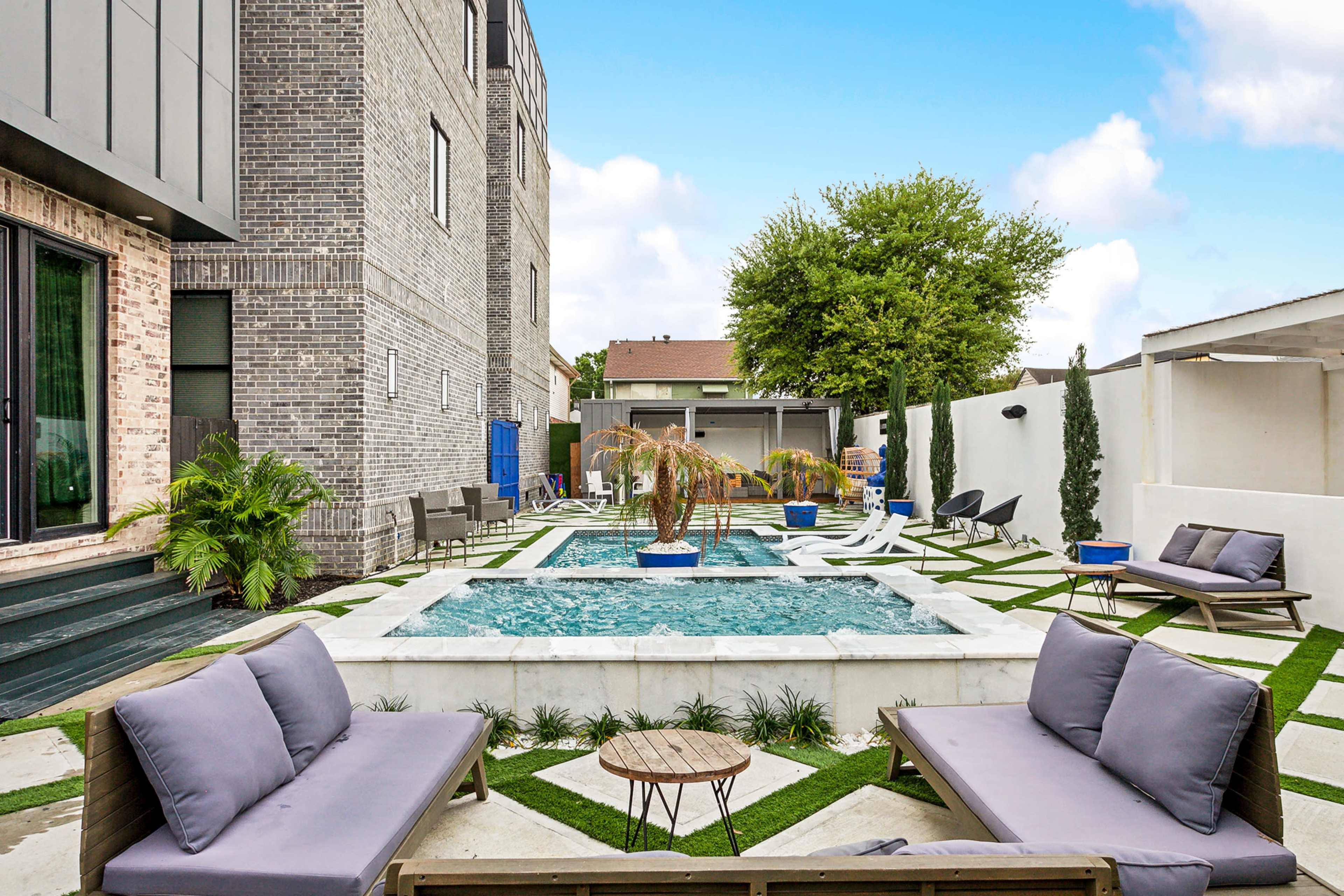 A modern outdoor space featuring a small pool surrounded by lounge chairs, a palm tree, and a well-maintained lawn.
