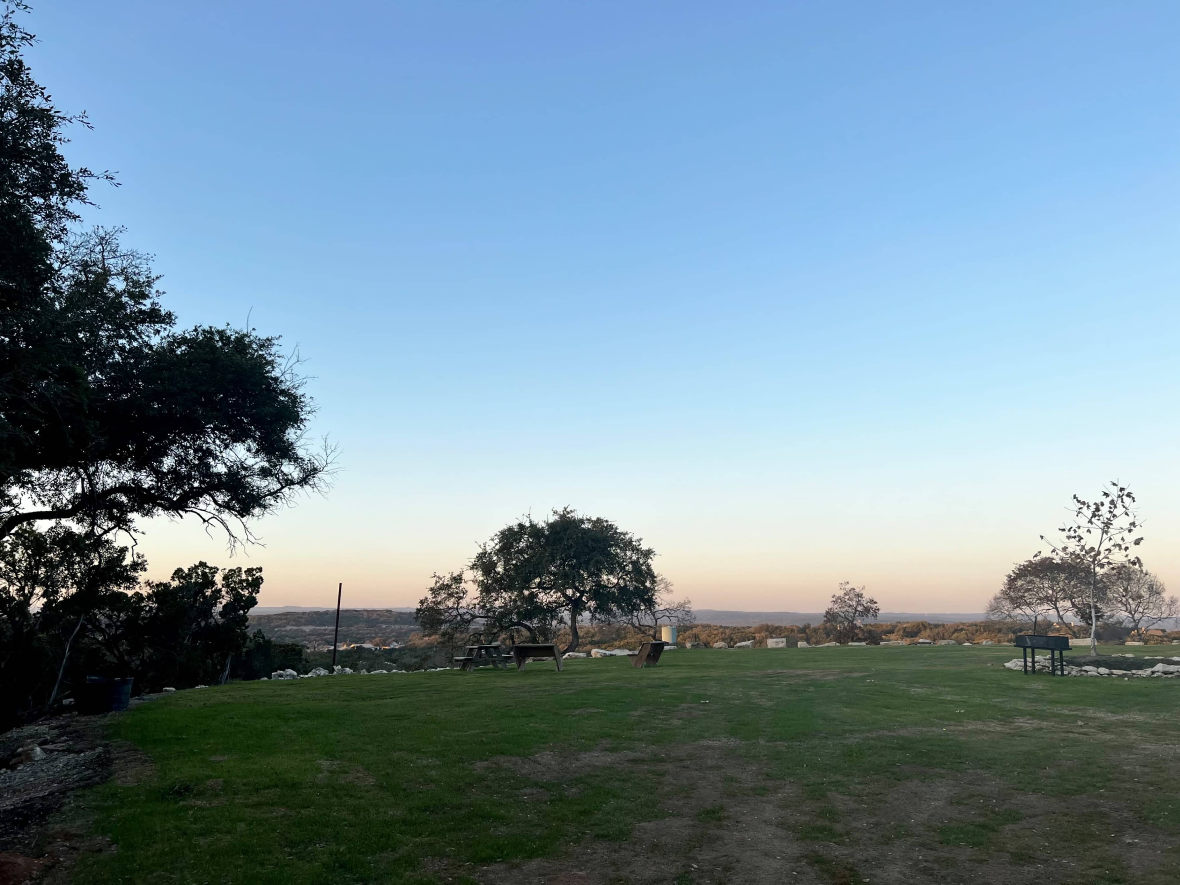 A green grassy area with scattered trees overlooks a distant landscape under a clear blue sky.