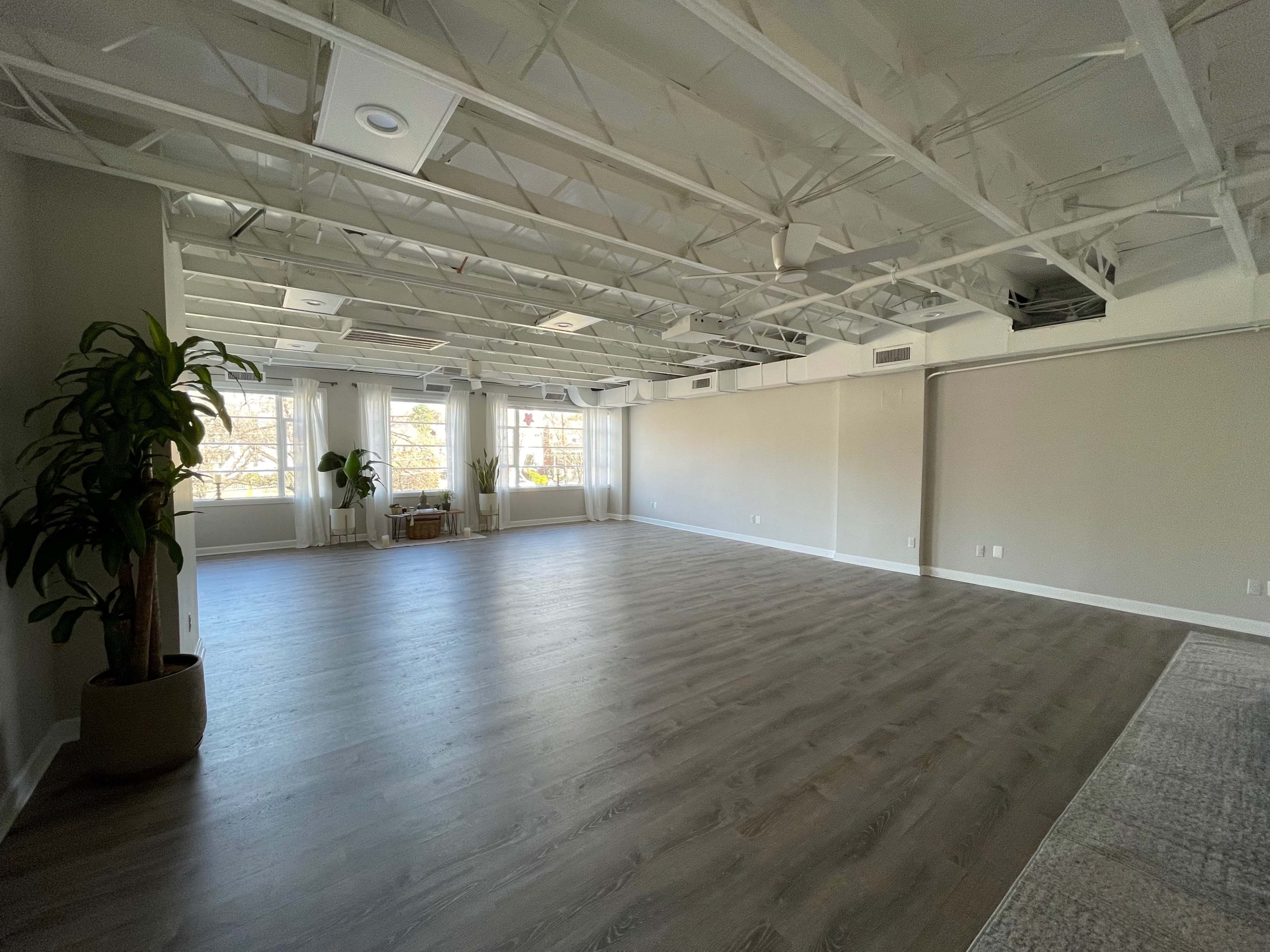A spacious, empty room with large windows, wooden flooring, and exposed ceiling beams.