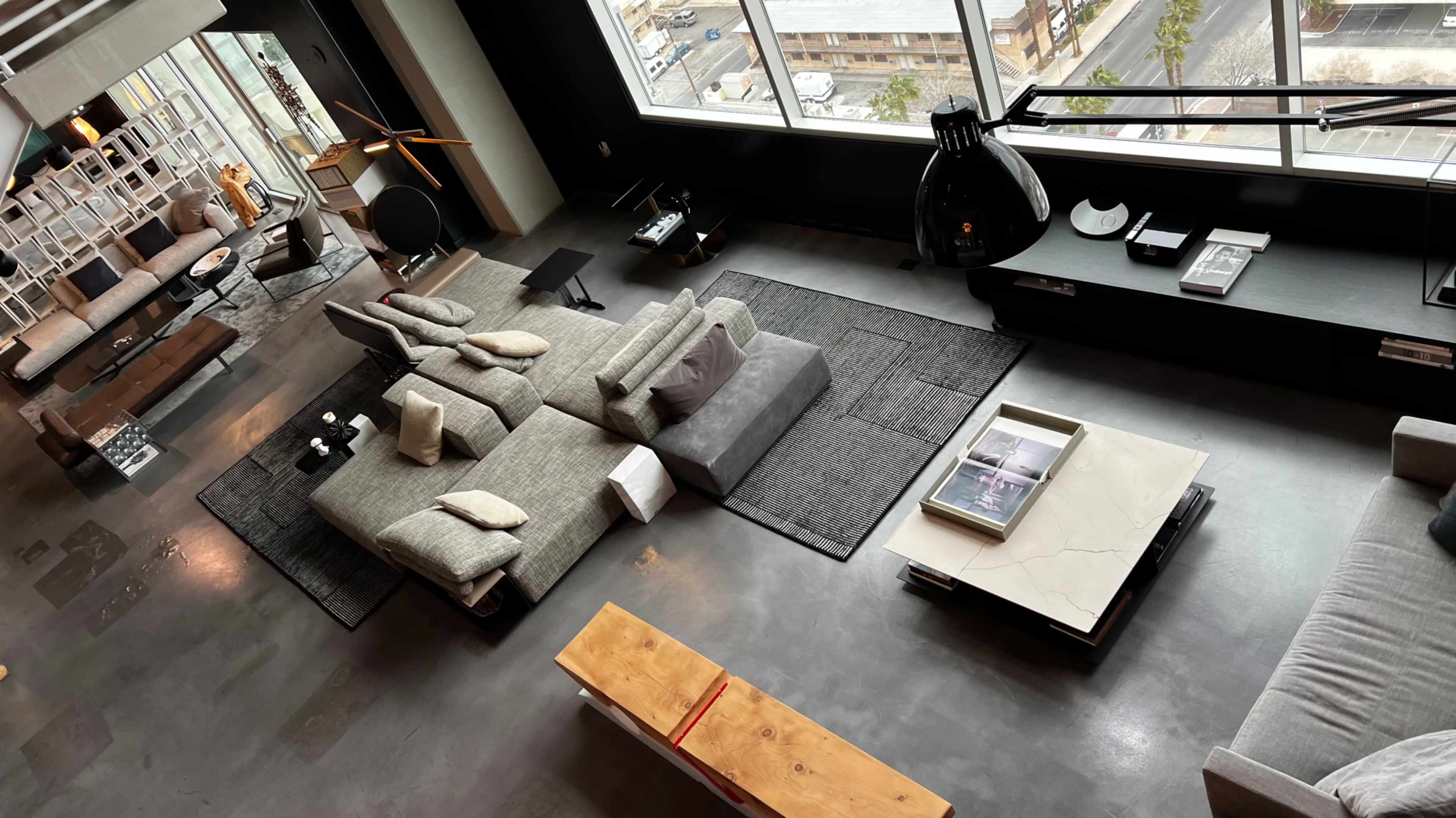 A modern living room with a large sectional sofa, a coffee table, and a prominent black floor lamp, all arranged around a central area rug near a large window.