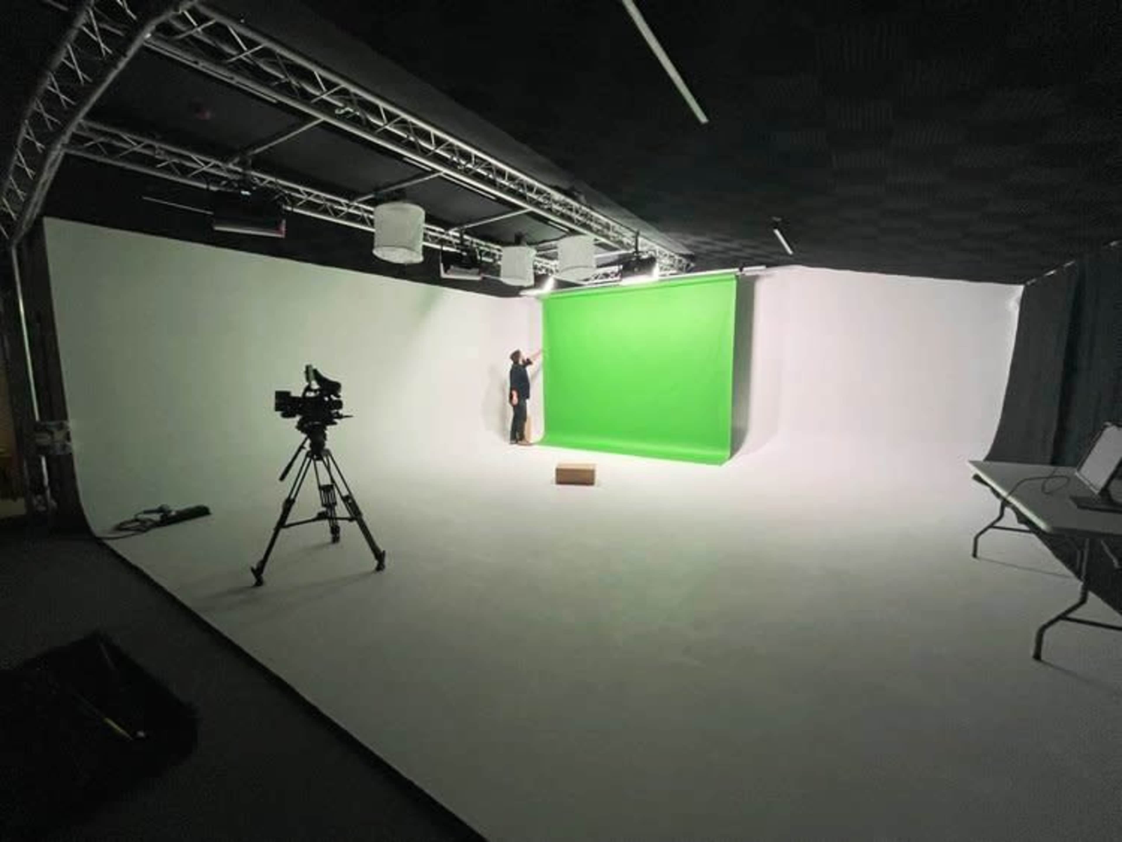 A person adjusts a green backdrop in a photography studio equipped with lighting and a camera.