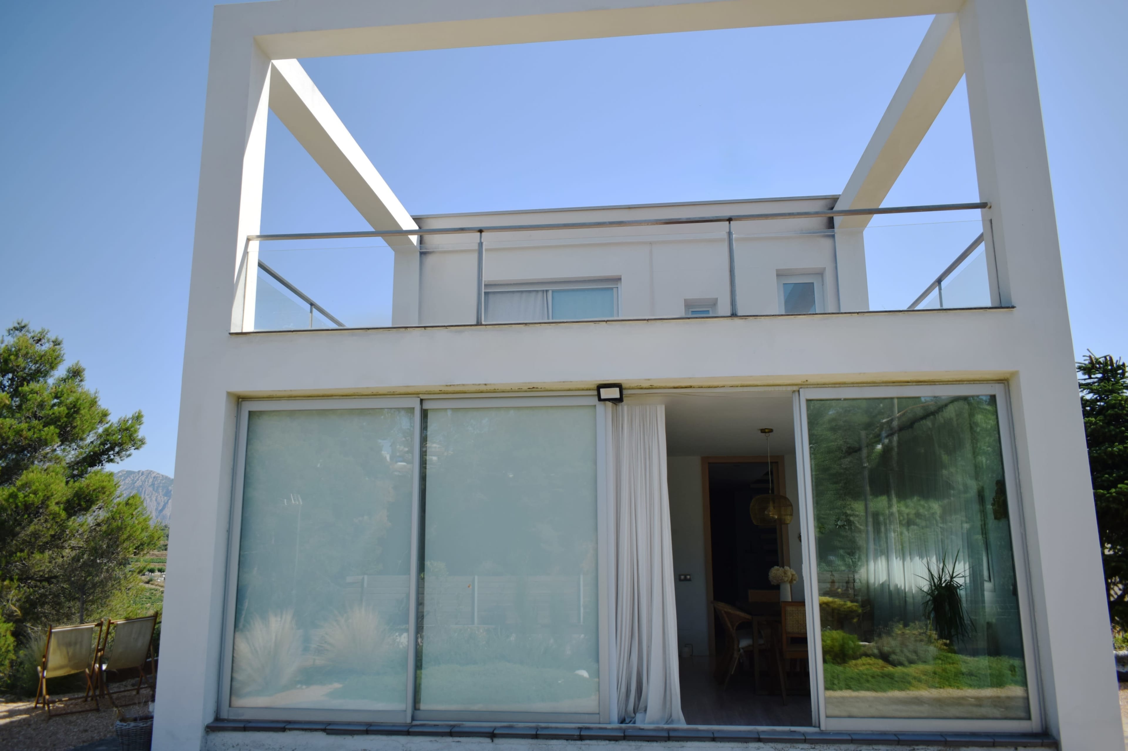 The image shows a modern two-story house with large glass windows and an exterior balcony on the upper level.