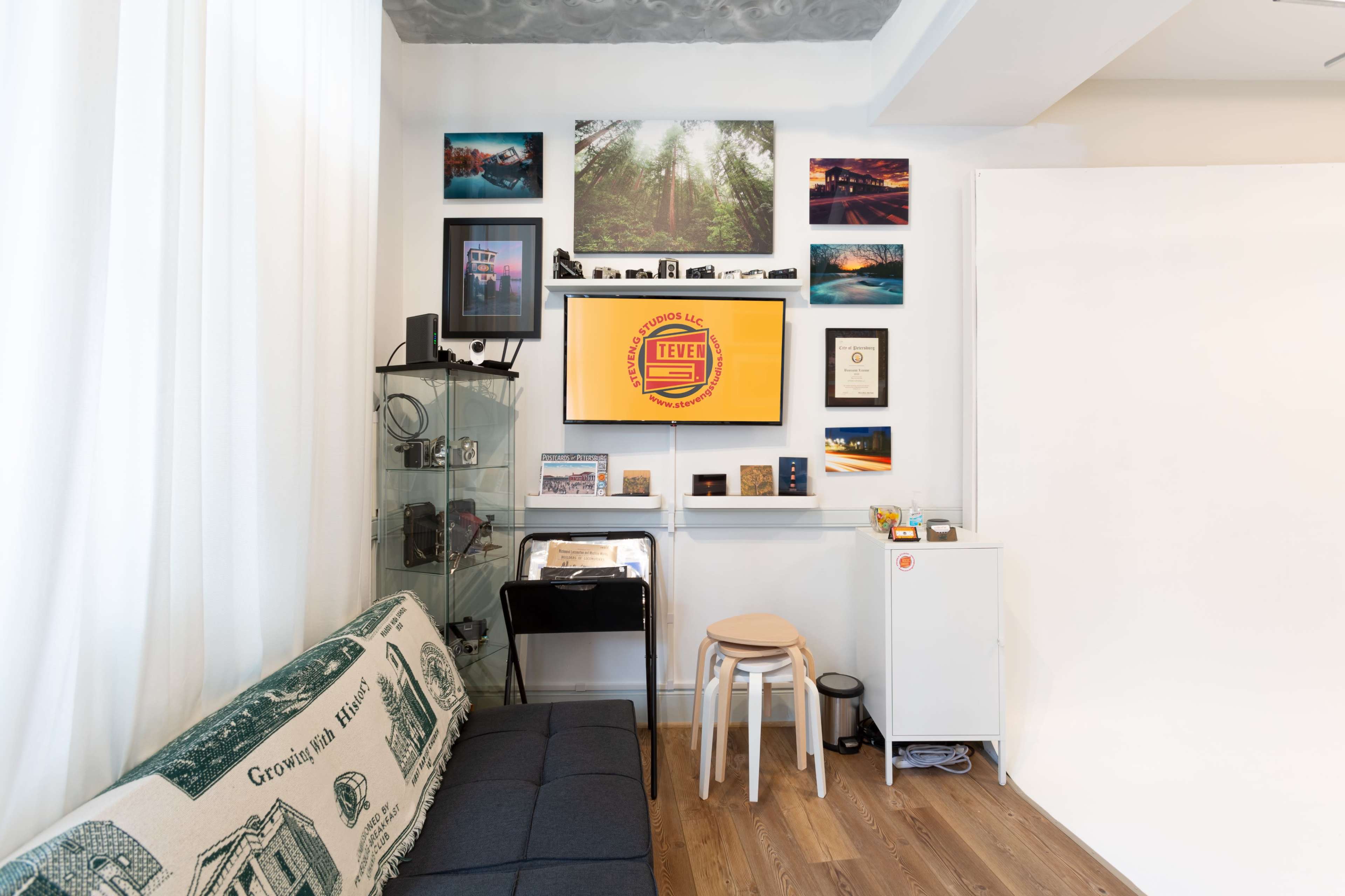 A cozy living space with a gray sofa, a television mounted on the wall, and various framed photographs and certificates displayed above a glass cabinet.