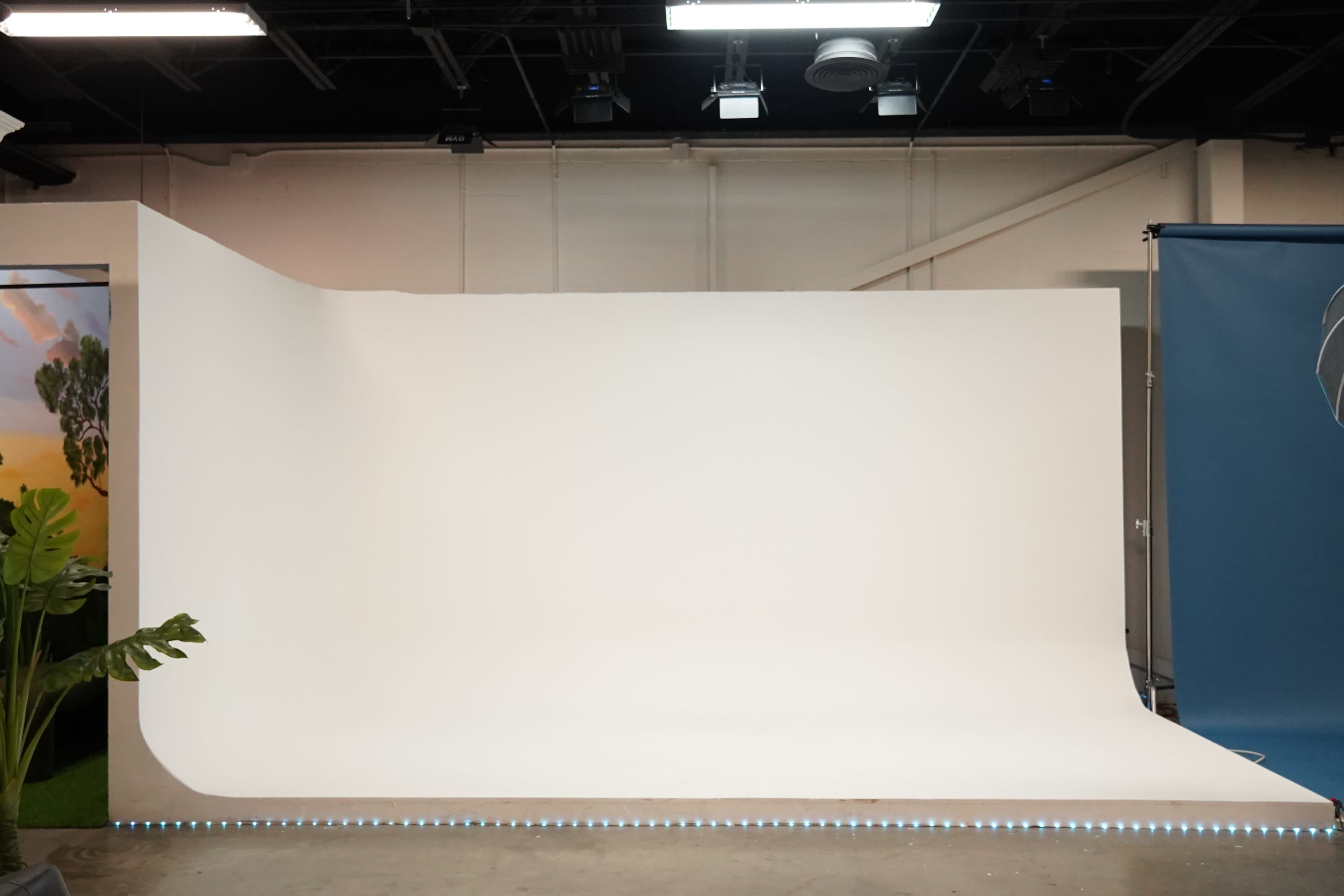 The image shows an empty photography studio with a large white backdrop and a soft curve at the base, illuminated by LED lights along the floor.