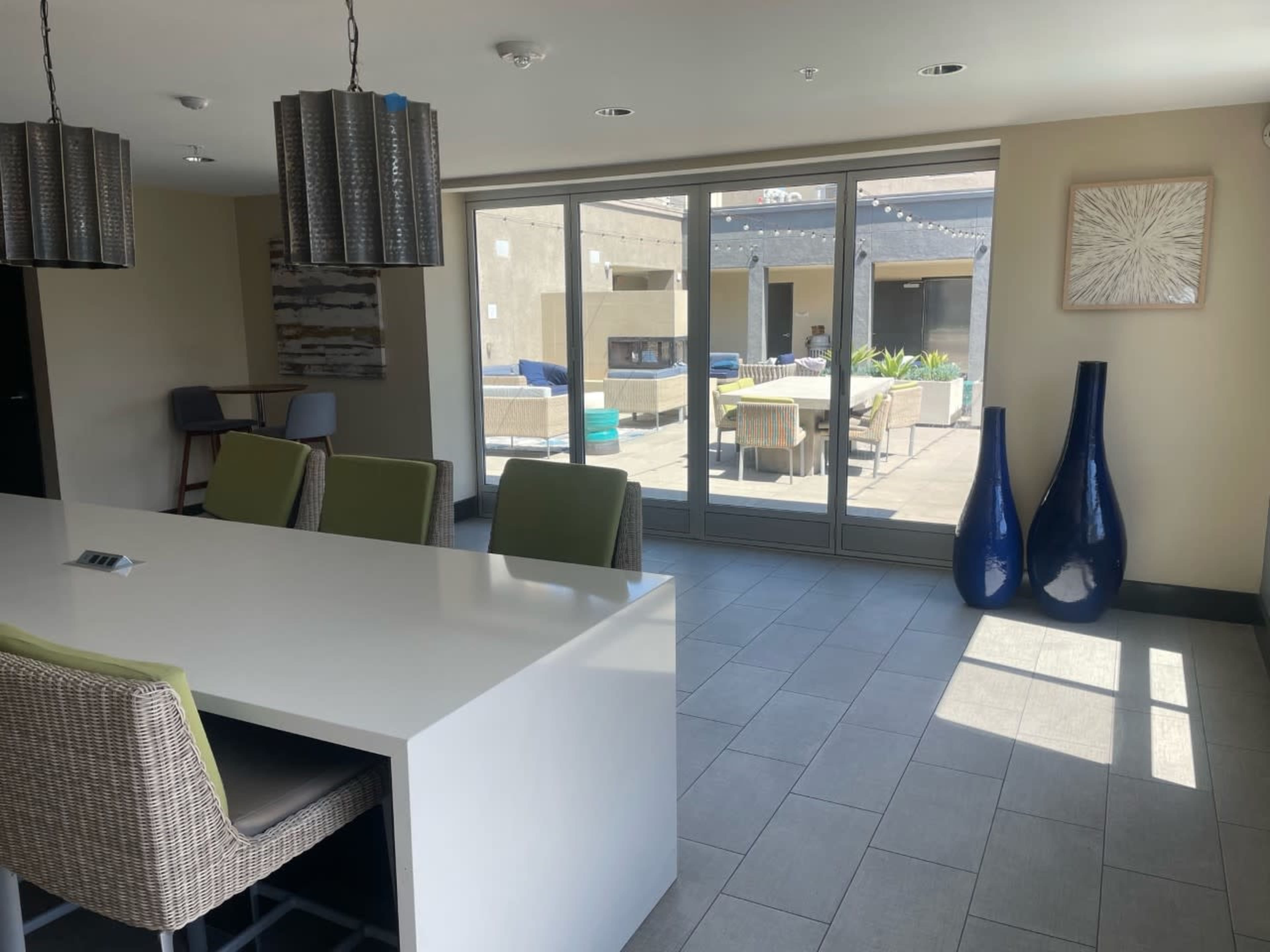 A modern indoor space with a long white table, green chairs, and large glass doors leading to an outdoor area with patio furniture and planters.