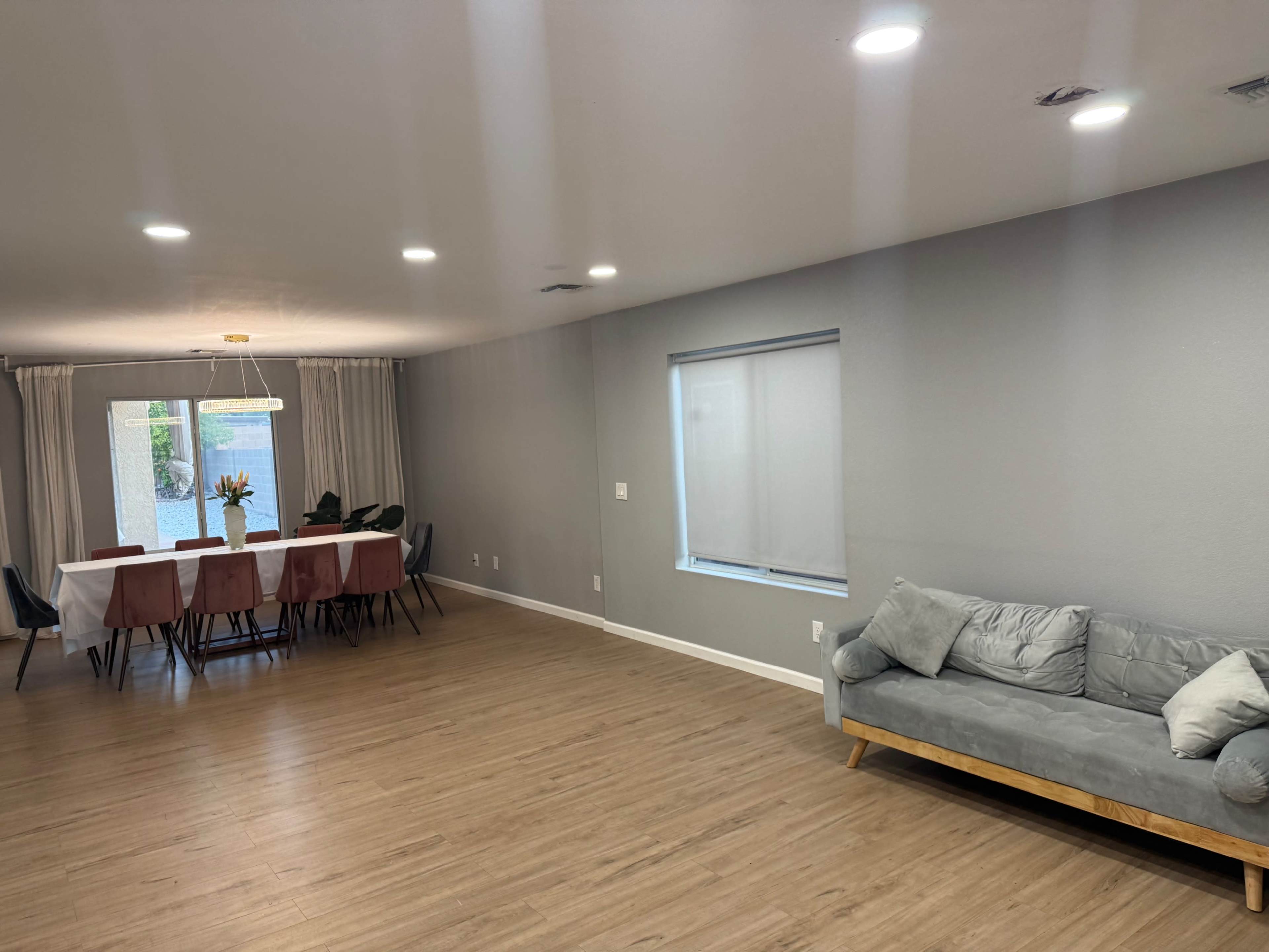 The image shows a spacious, modern living area with a dining table set for six and a gray sofa against a wall.