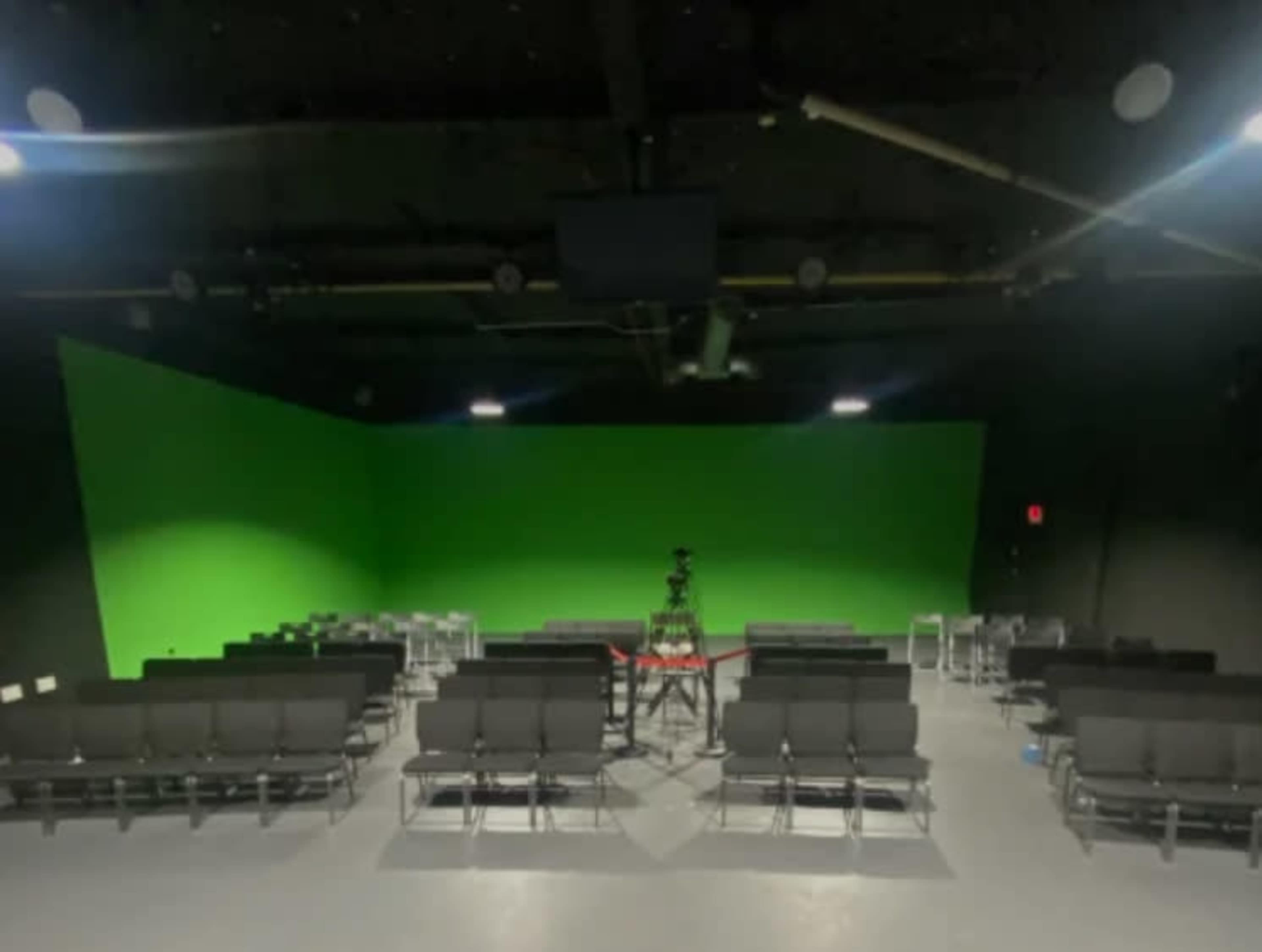 An empty studio space with rows of chairs facing a green screen backdrop.