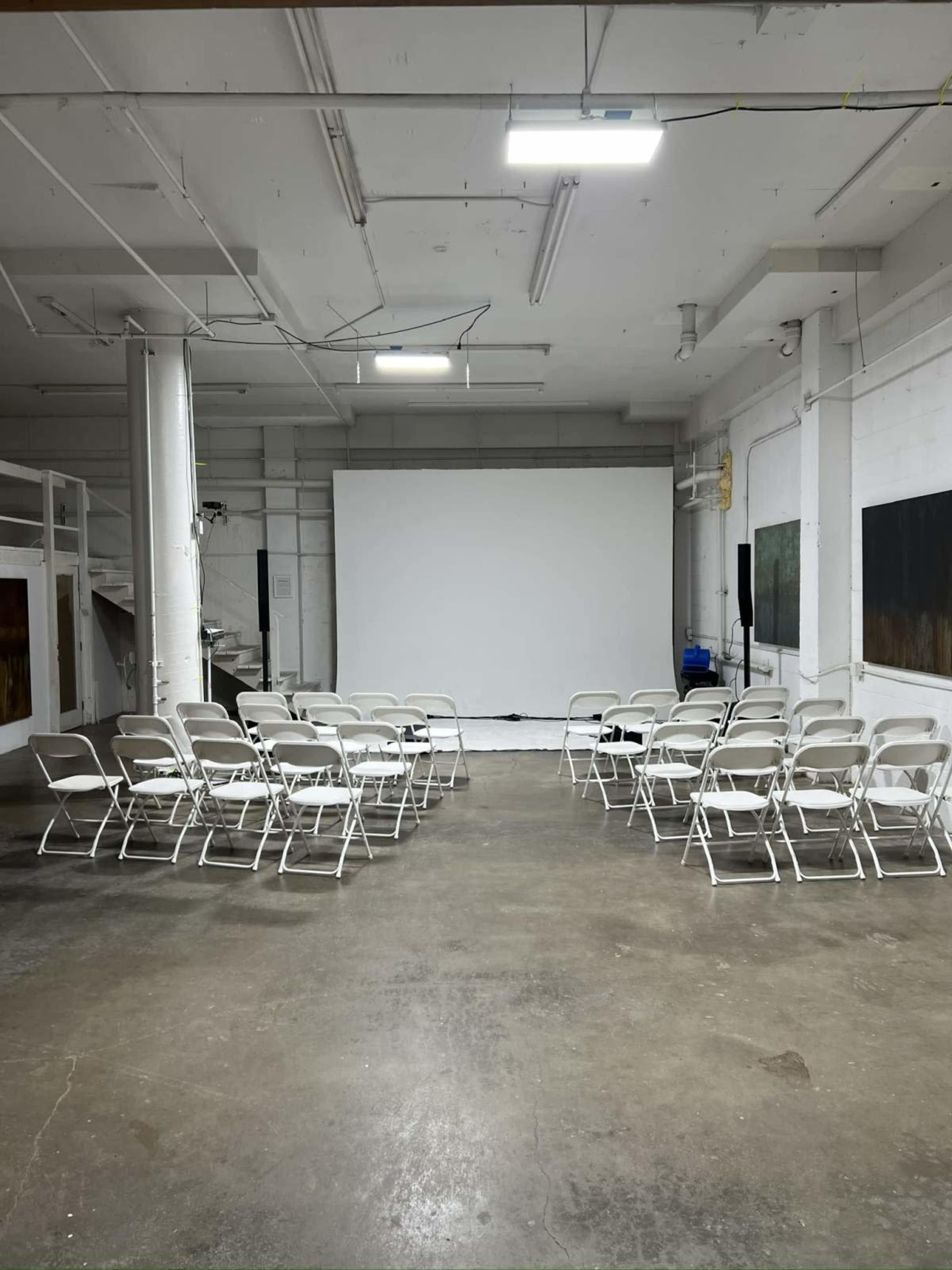 The image shows a spacious, empty room with rows of white chairs facing a large blank screen.
