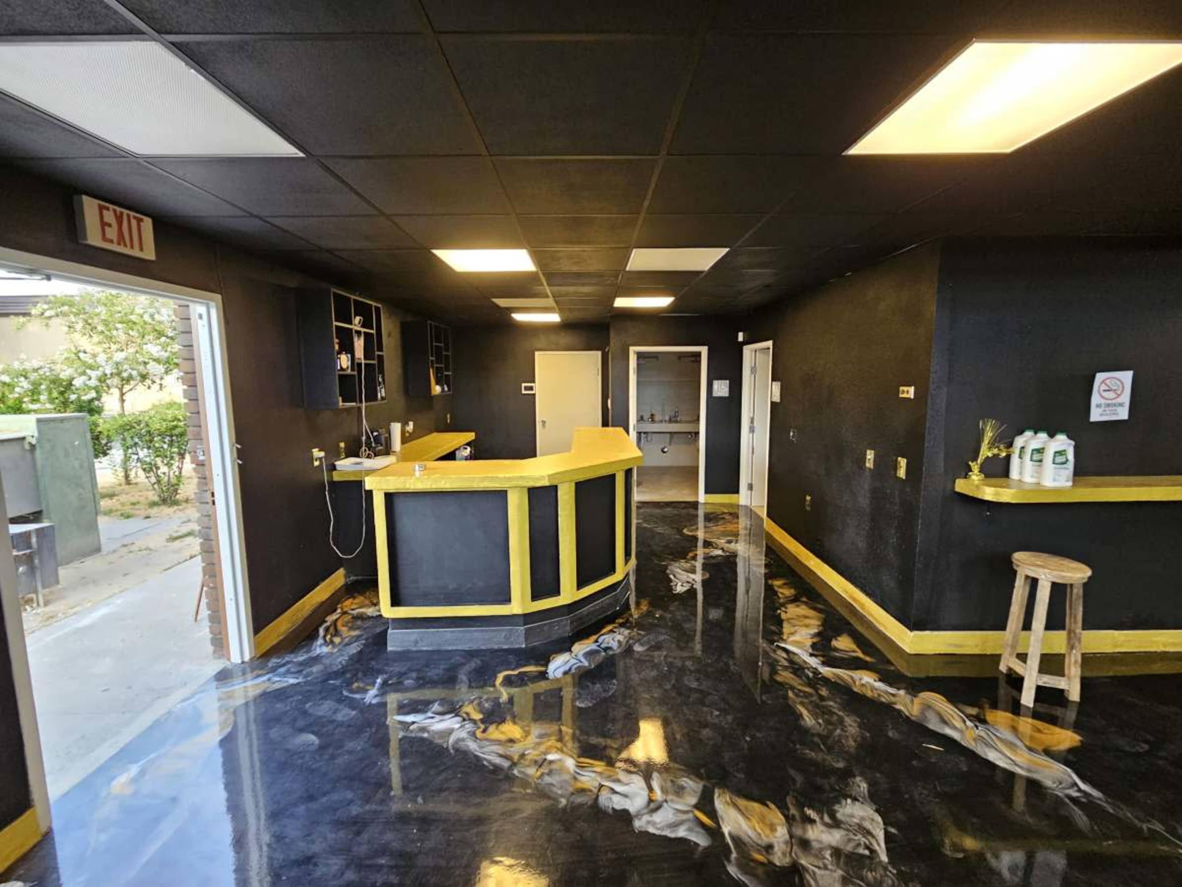 The image shows a modern interior of a room with a yellow and black color scheme, featuring a reception desk, black walls, and shiny, patterned flooring.
