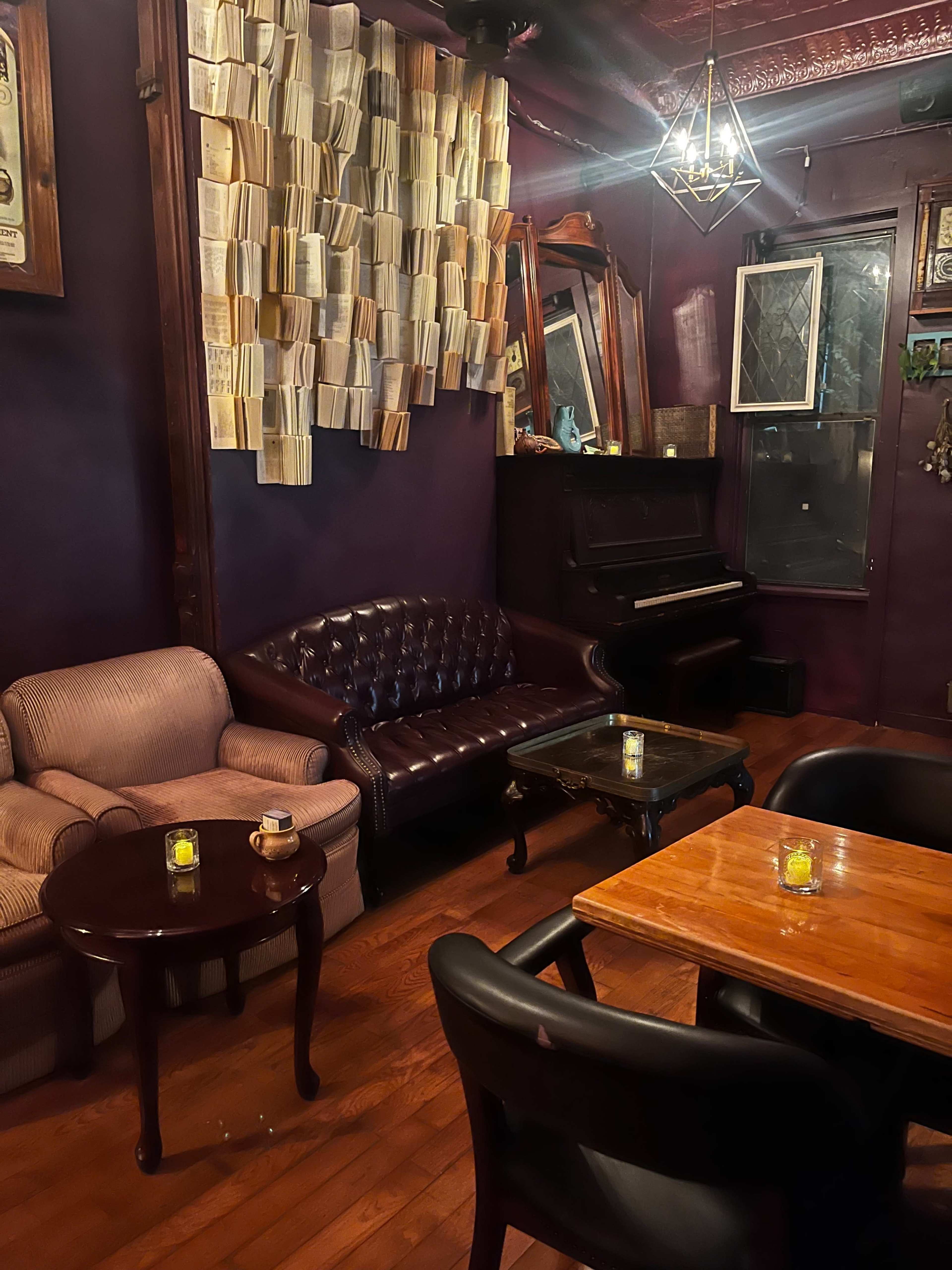 A cozy cafe interior with a mix of plush seating, a piano, and decor featuring hanging books.