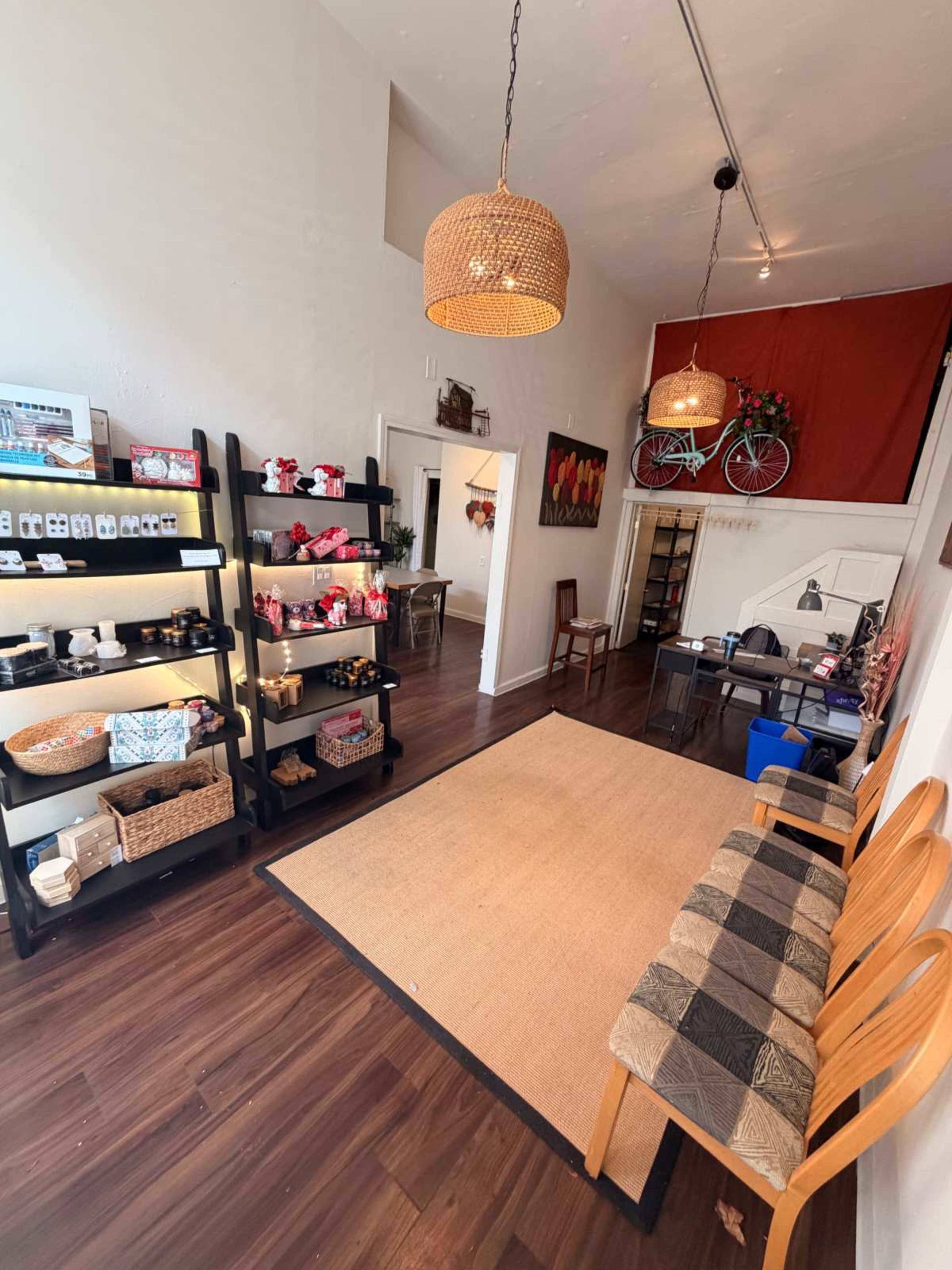 The image shows a well-organized retail space featuring shelves of products, a seating area with wooden chairs, and an office area in the back.