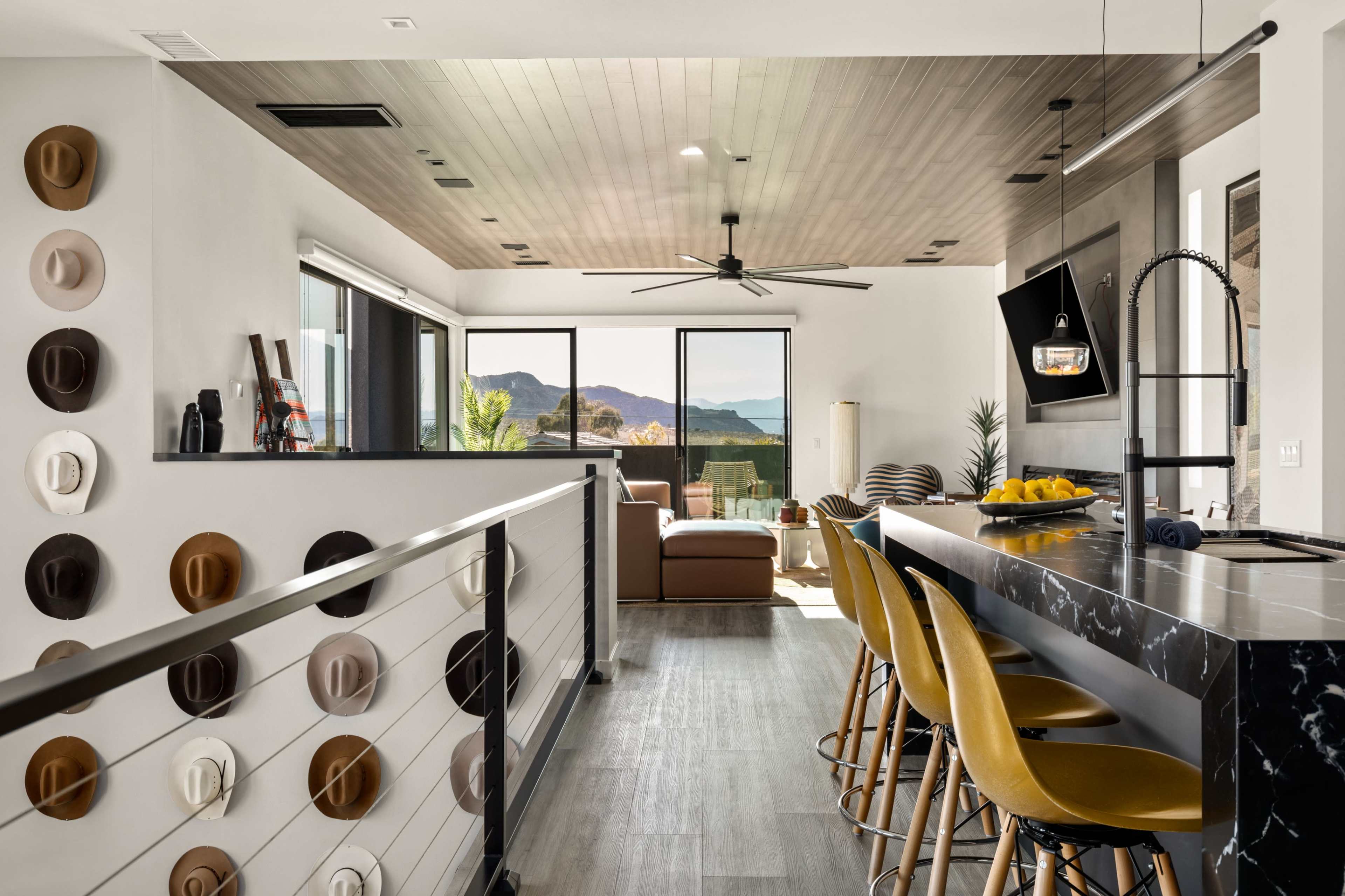 The image shows a modern interior space featuring a kitchen and living area with a view of mountains through large windows.