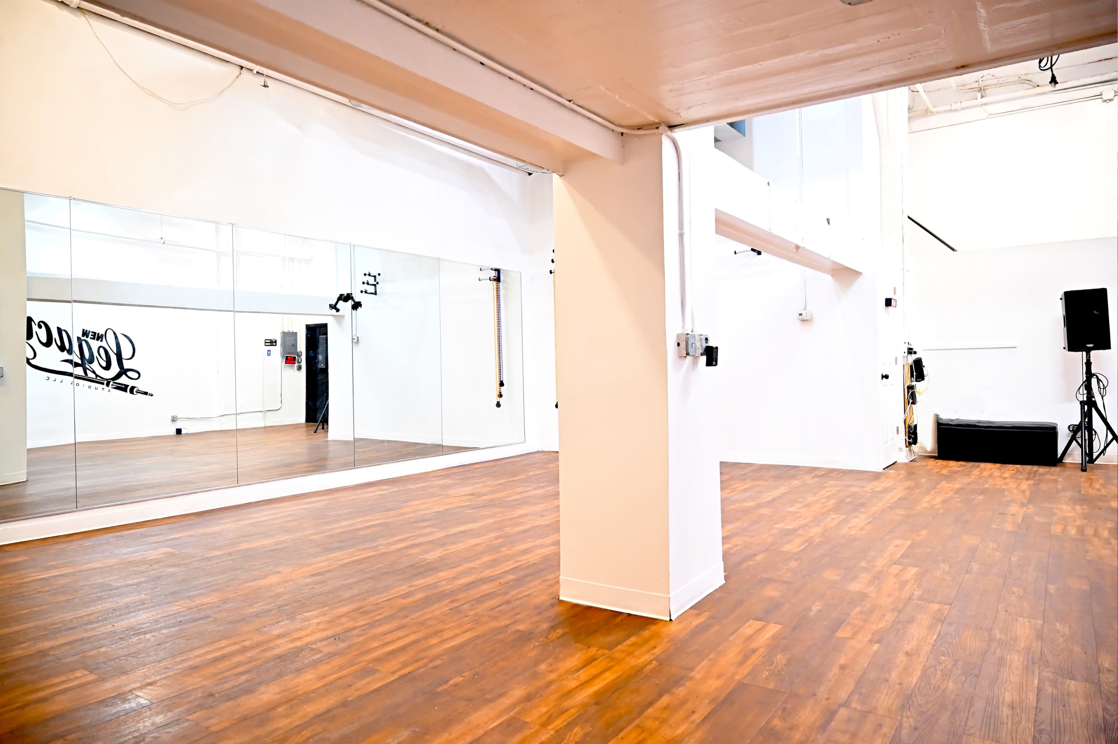 A spacious, well-lit studio with wooden flooring, a large mirror on one wall, and minimalistic decor.