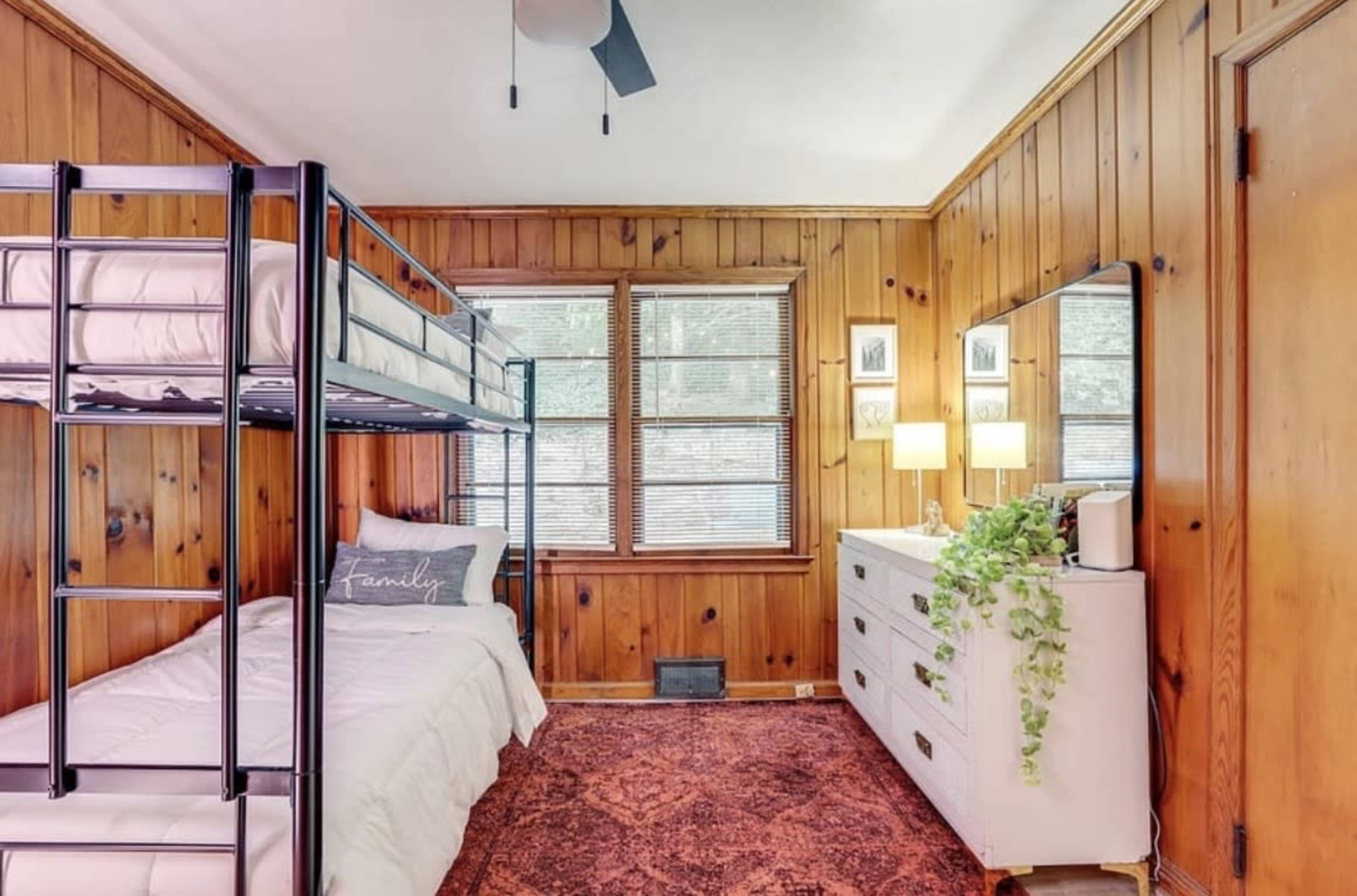 The image depicts a wooden-paneled bedroom featuring a bunk bed, a dresser, and a cozy area rug.