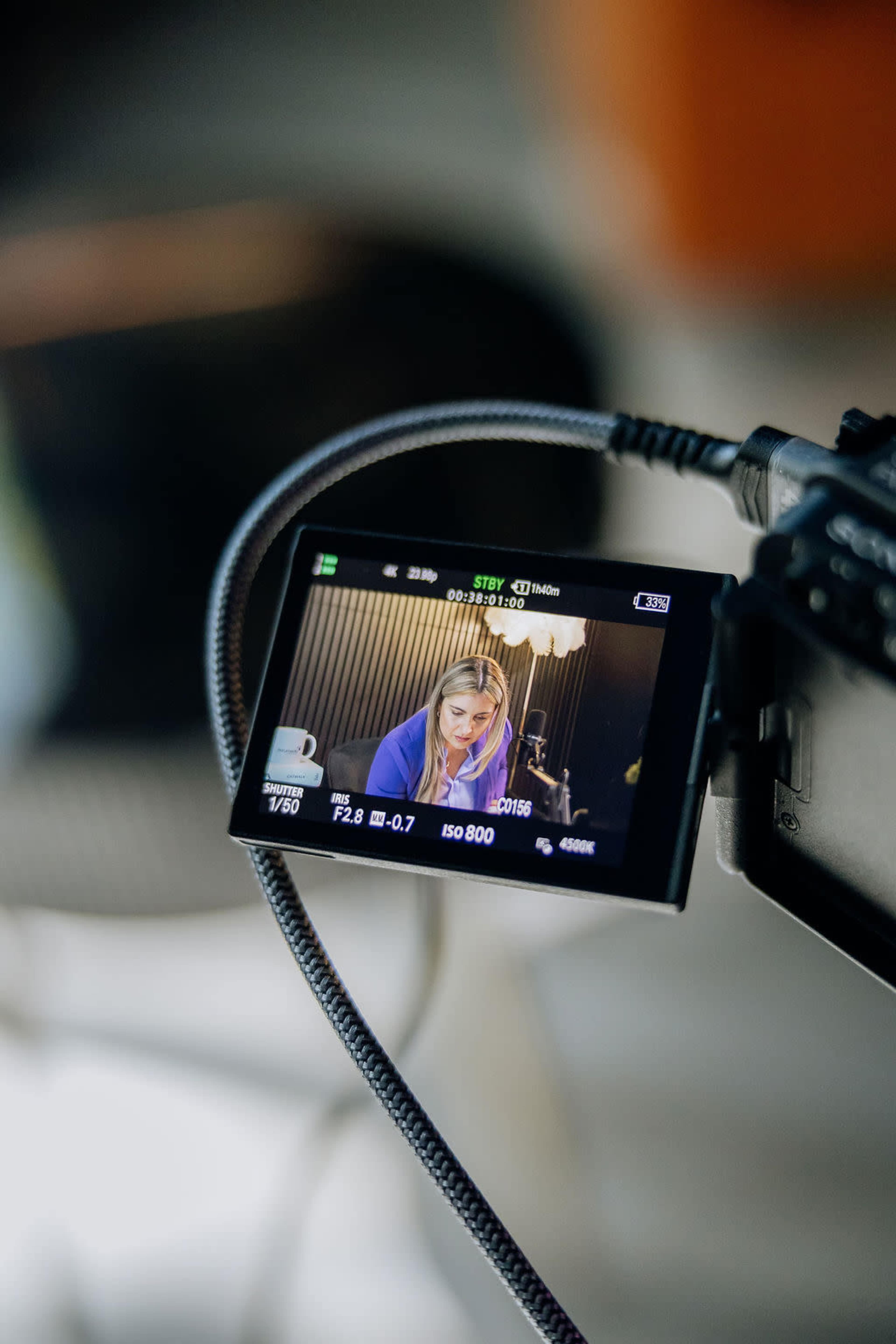 The image shows a camera display with a woman being recorded, while the camera is set up on a stand.
