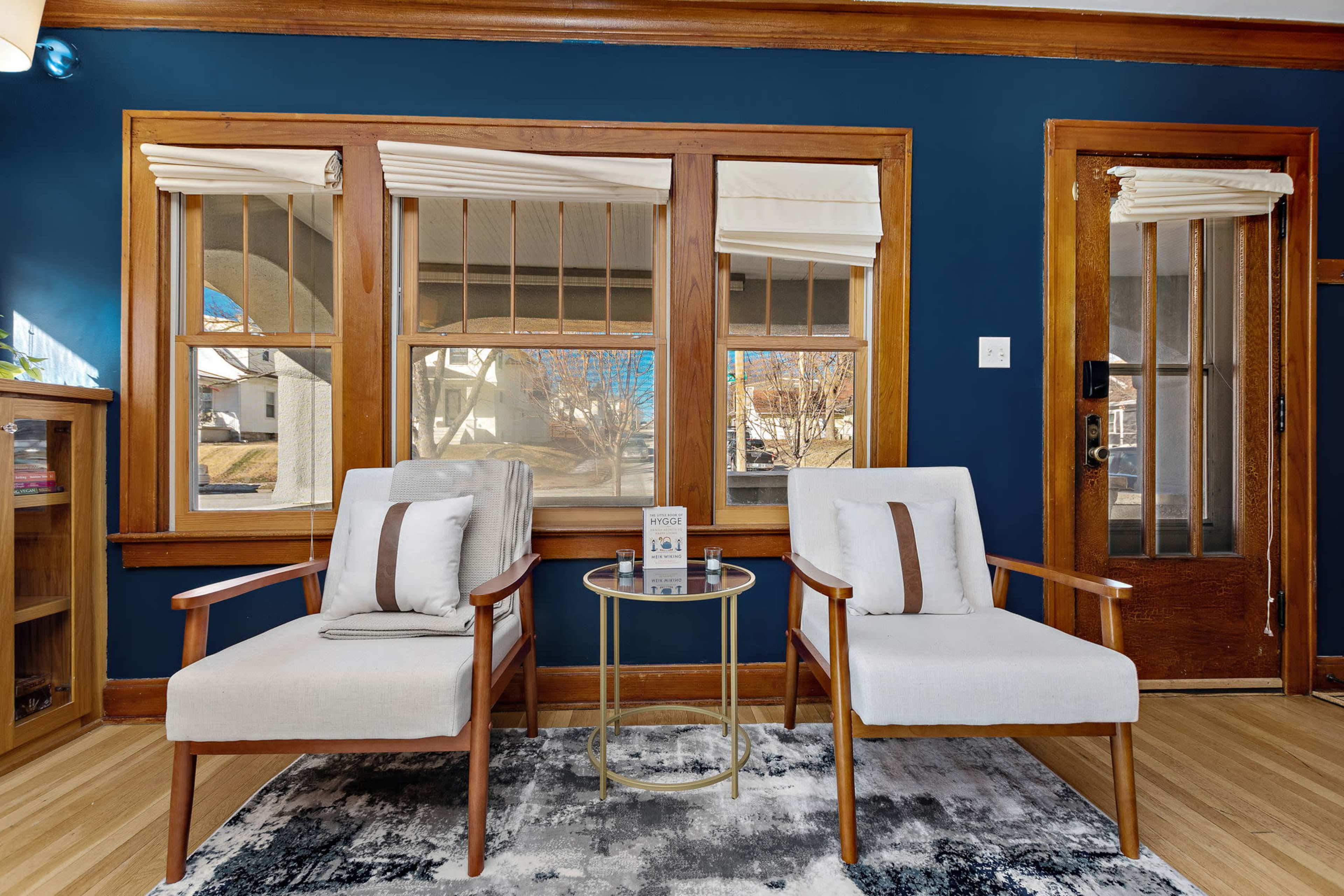 A cozy seating area with two upholstered chairs, a small round table between them, and large windows with wooden frames that let in natural light.