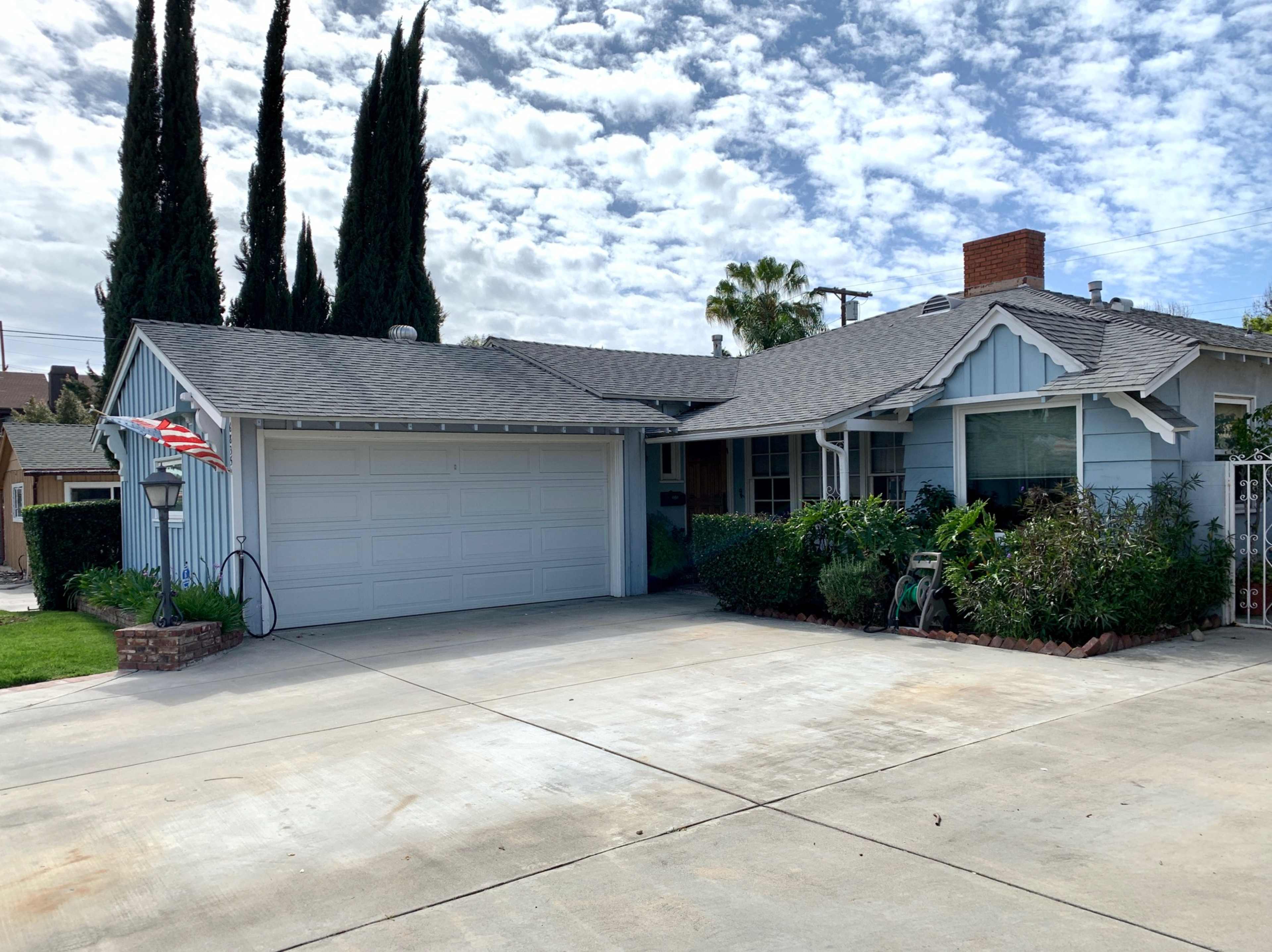 A single-story, light blue house with a garage and a neatly kept front yard under a partly cloudy sky.