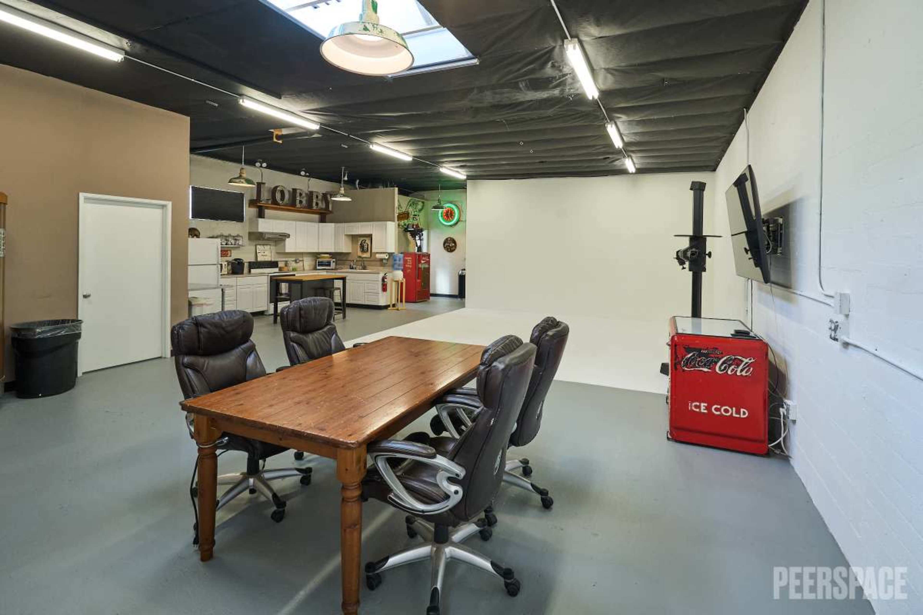 The image shows a spacious, well-lit studio with a white backdrop and a wooden conference table surrounded by black chairs.