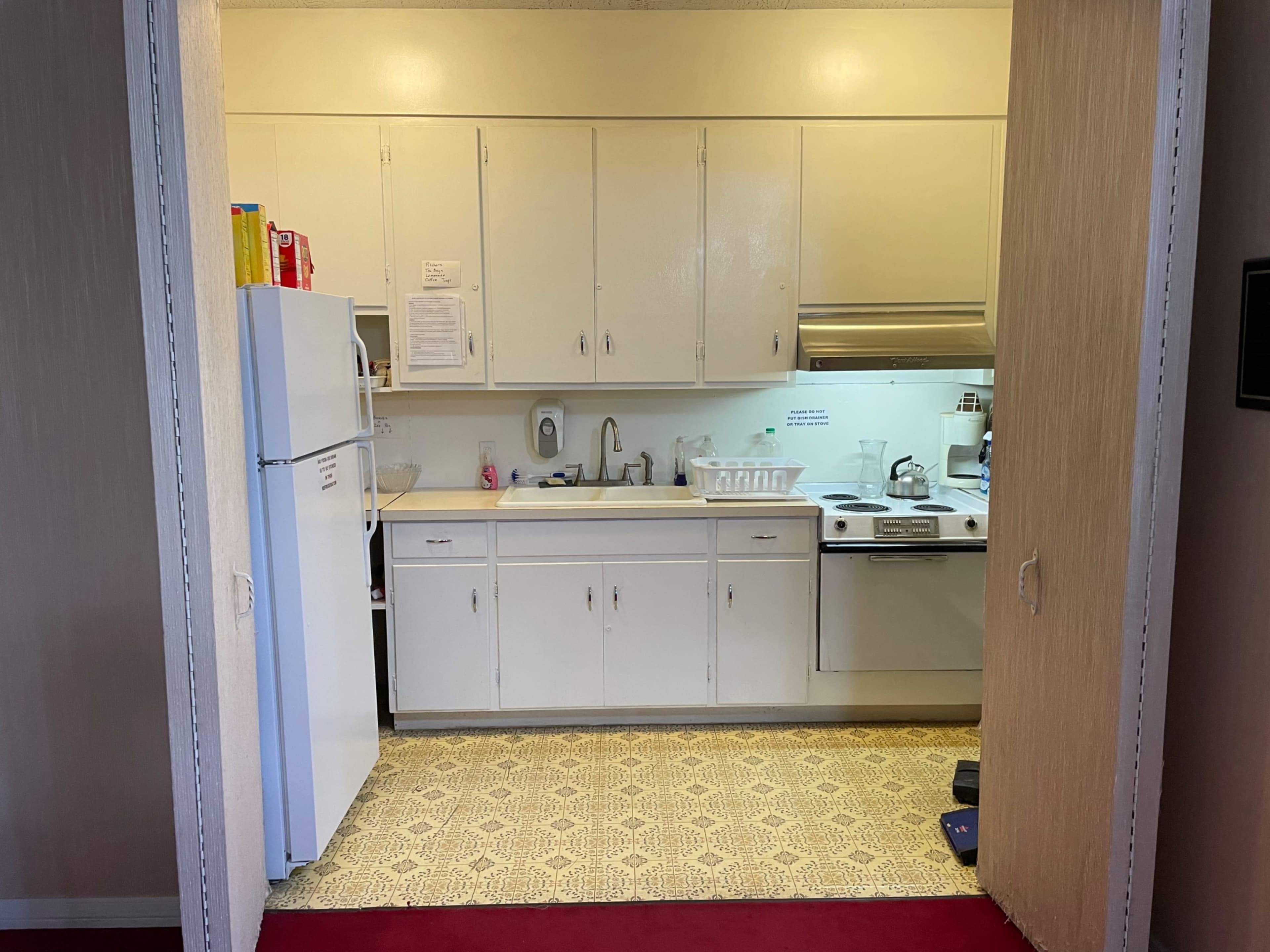 A compact kitchen with white cabinets, a sink, stove, and refrigerator is visible through an open doorway.