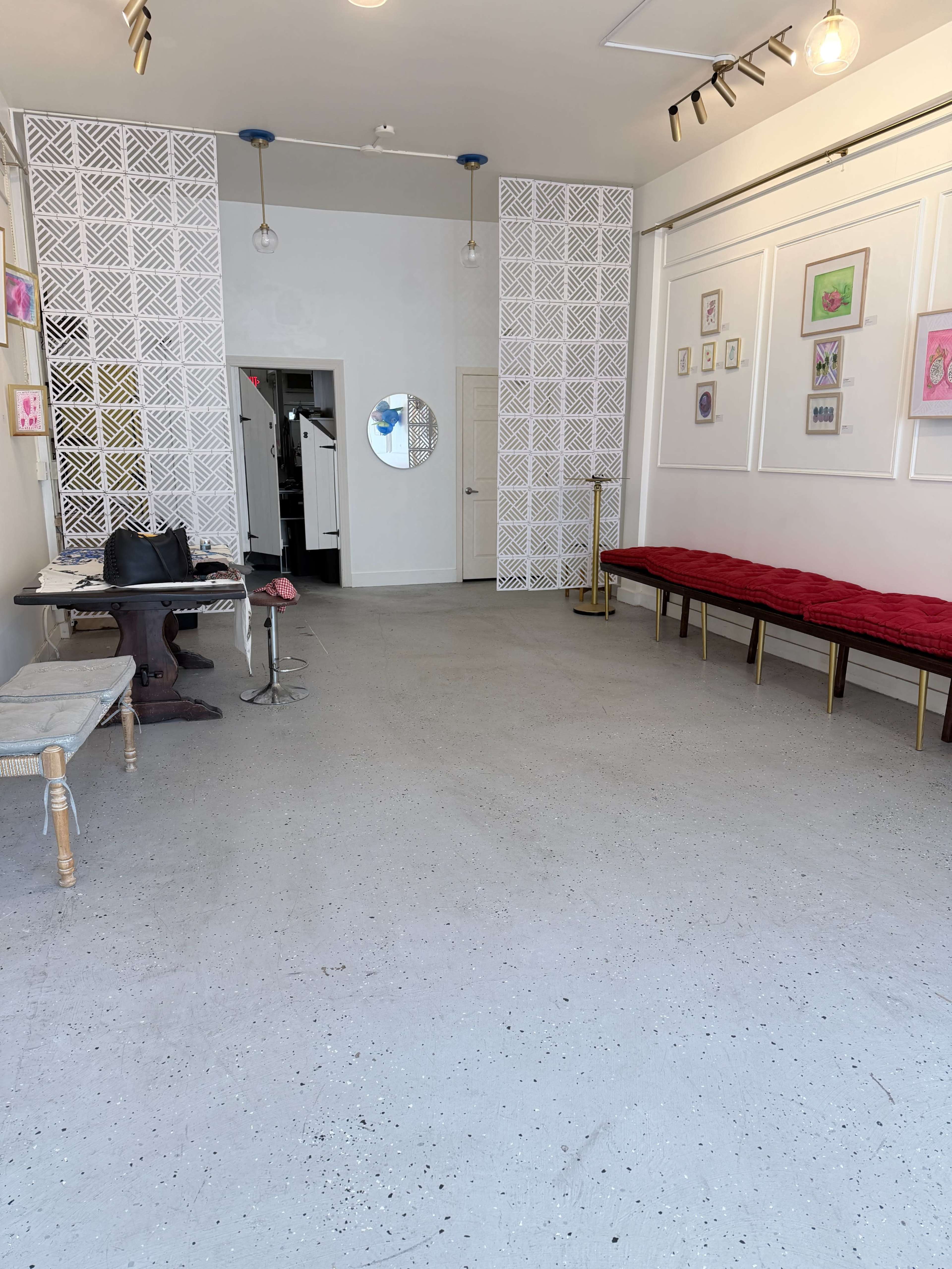 The image shows an empty, well-lit interior space with light gray flooring, decorated walls, and a bench along one side.