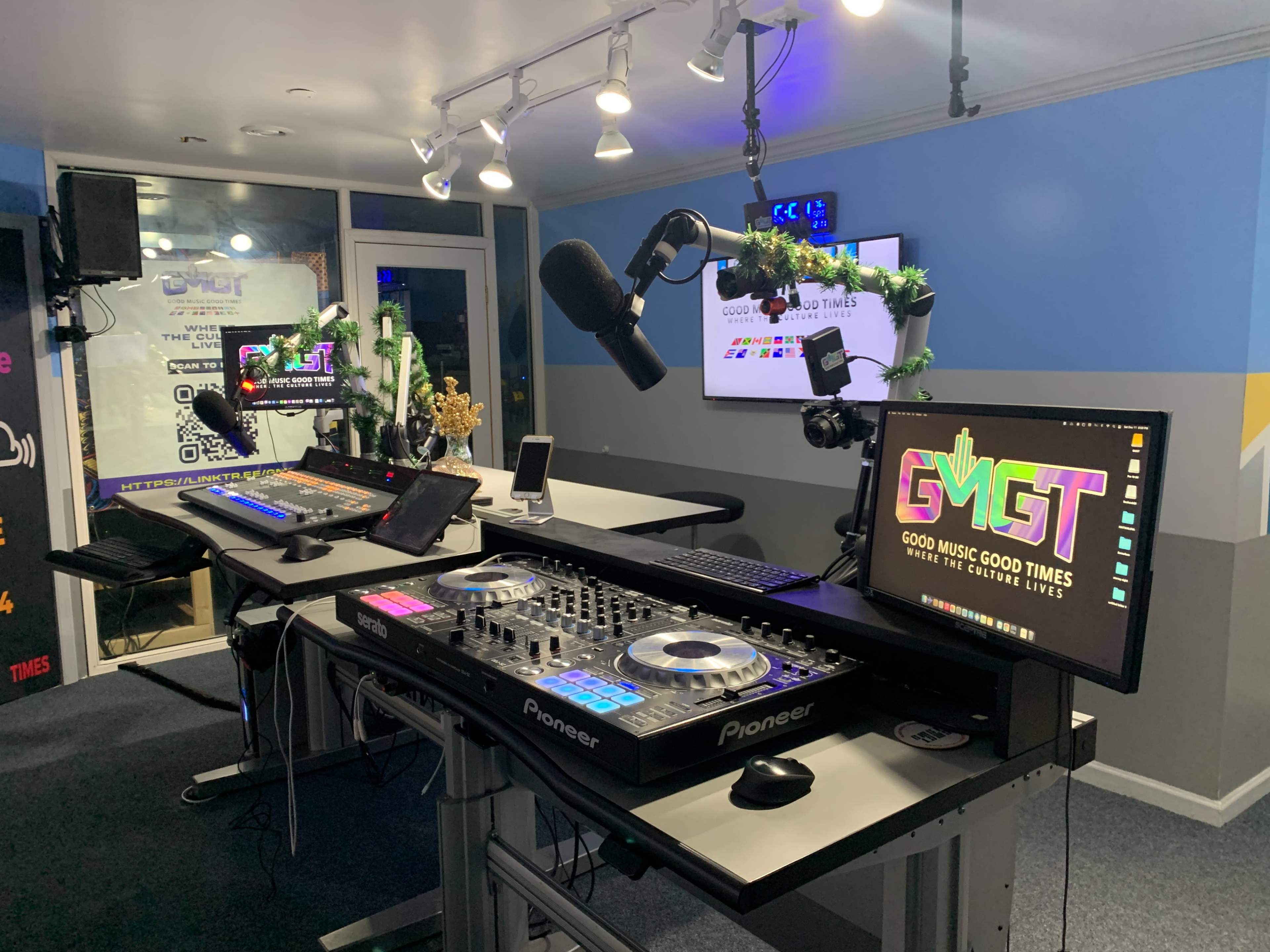 The image shows a modern DJ setup featuring Pioneer equipment and two large screens displaying the logo "GMGT" in a brightly lit room.