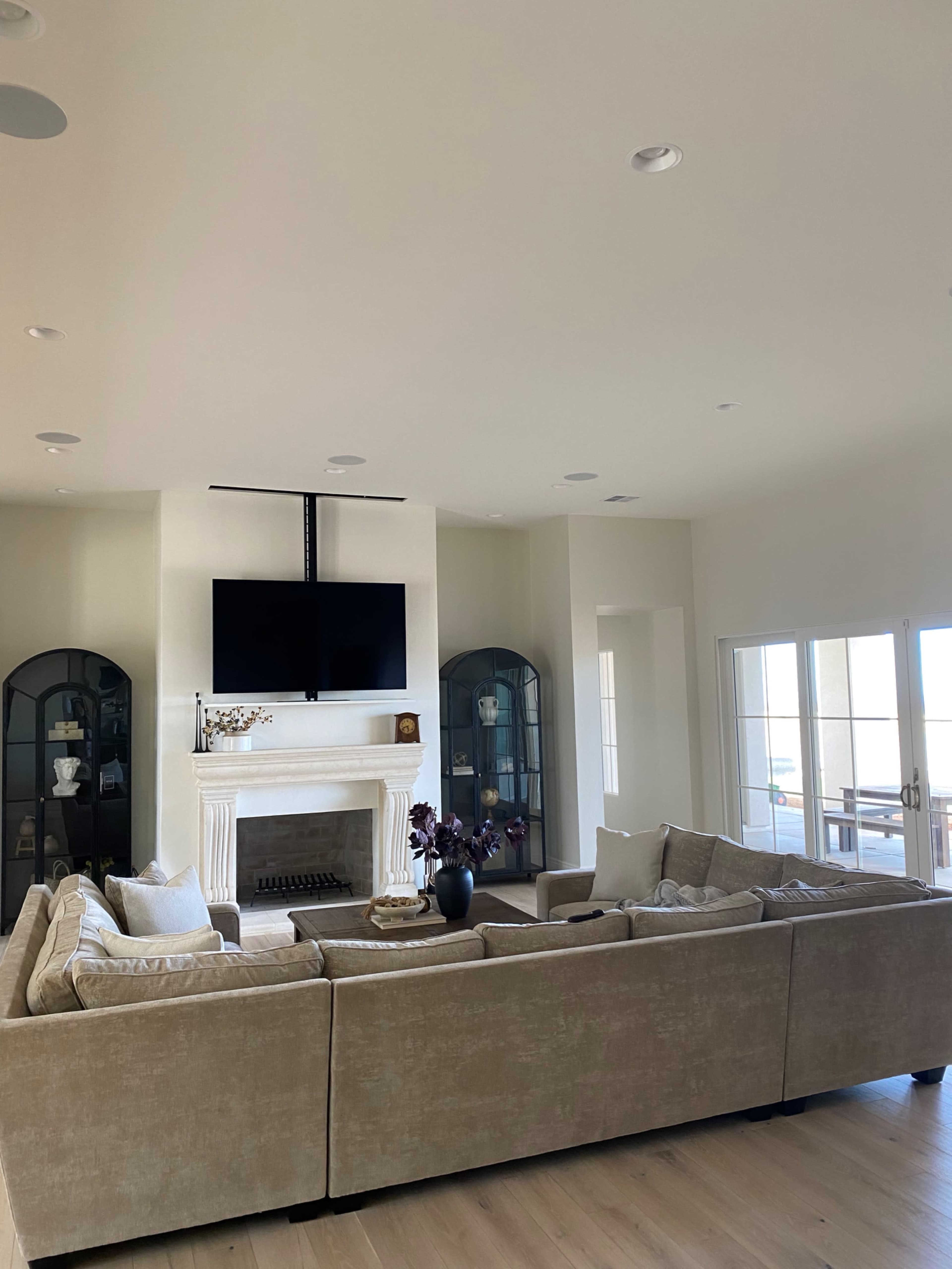 A spacious living room featuring a large sectional sofa, a mounted television above a white fireplace, and two glass display cabinets on either side.