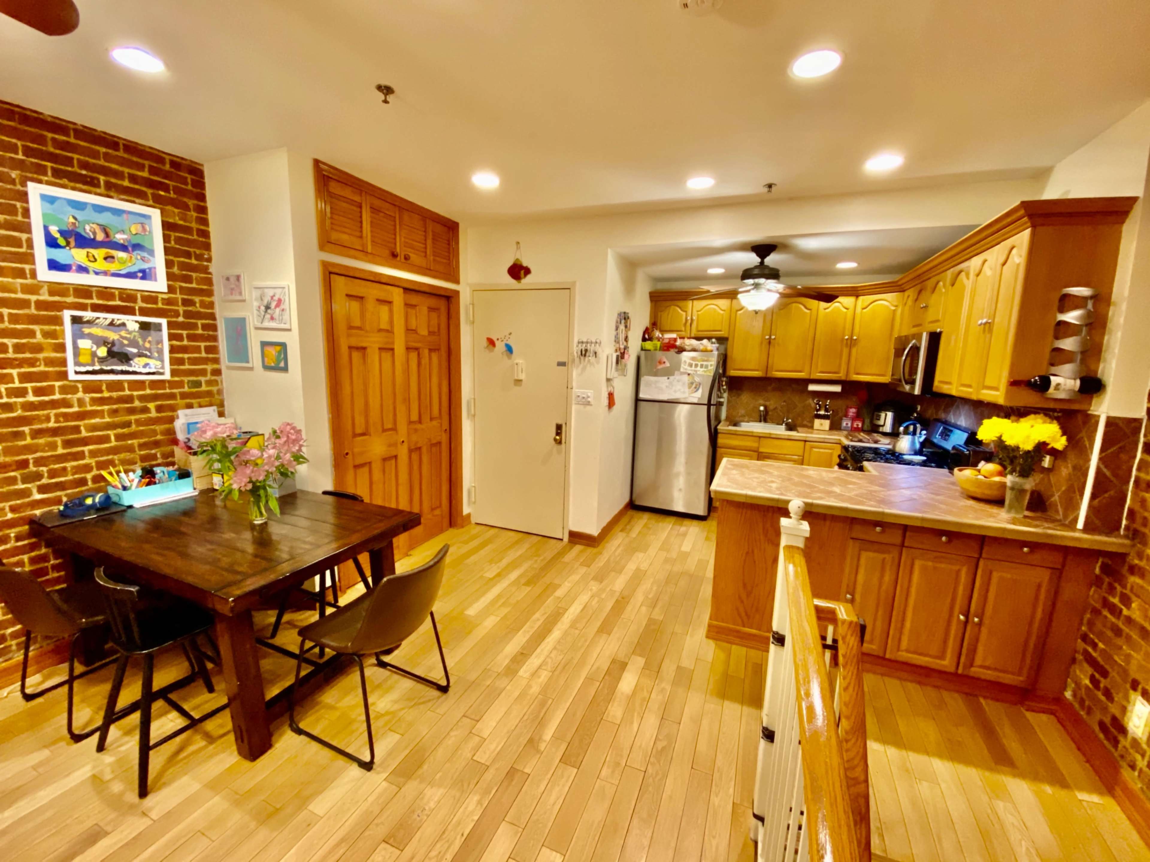 A kitchen and dining area with wooden floors, brick walls, and a table with chairs near a fully-equipped kitchen featuring wooden cabinets and appliances.