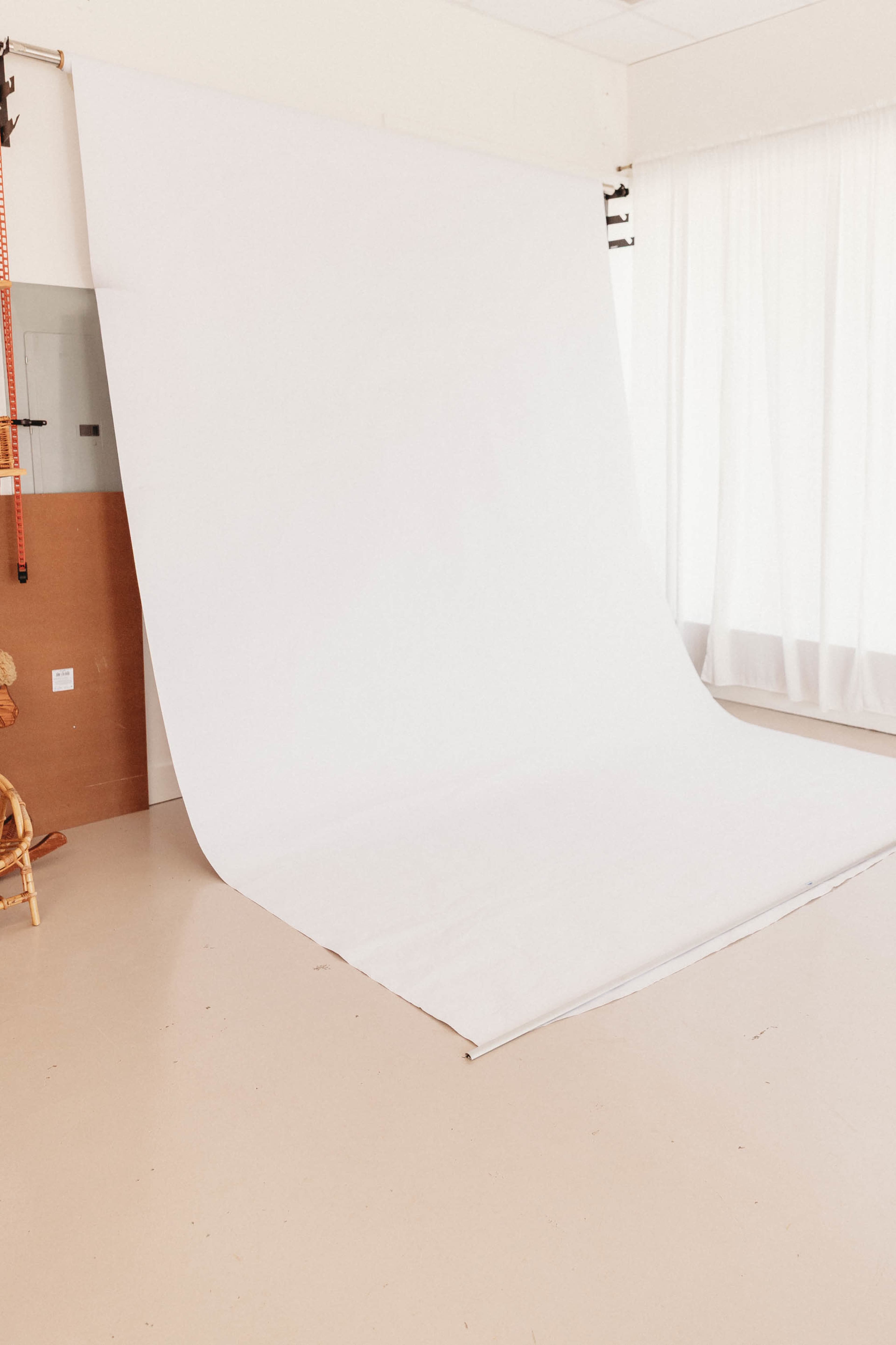 The image shows an empty photography studio with a large white backdrop and soft natural light illuminating the space.