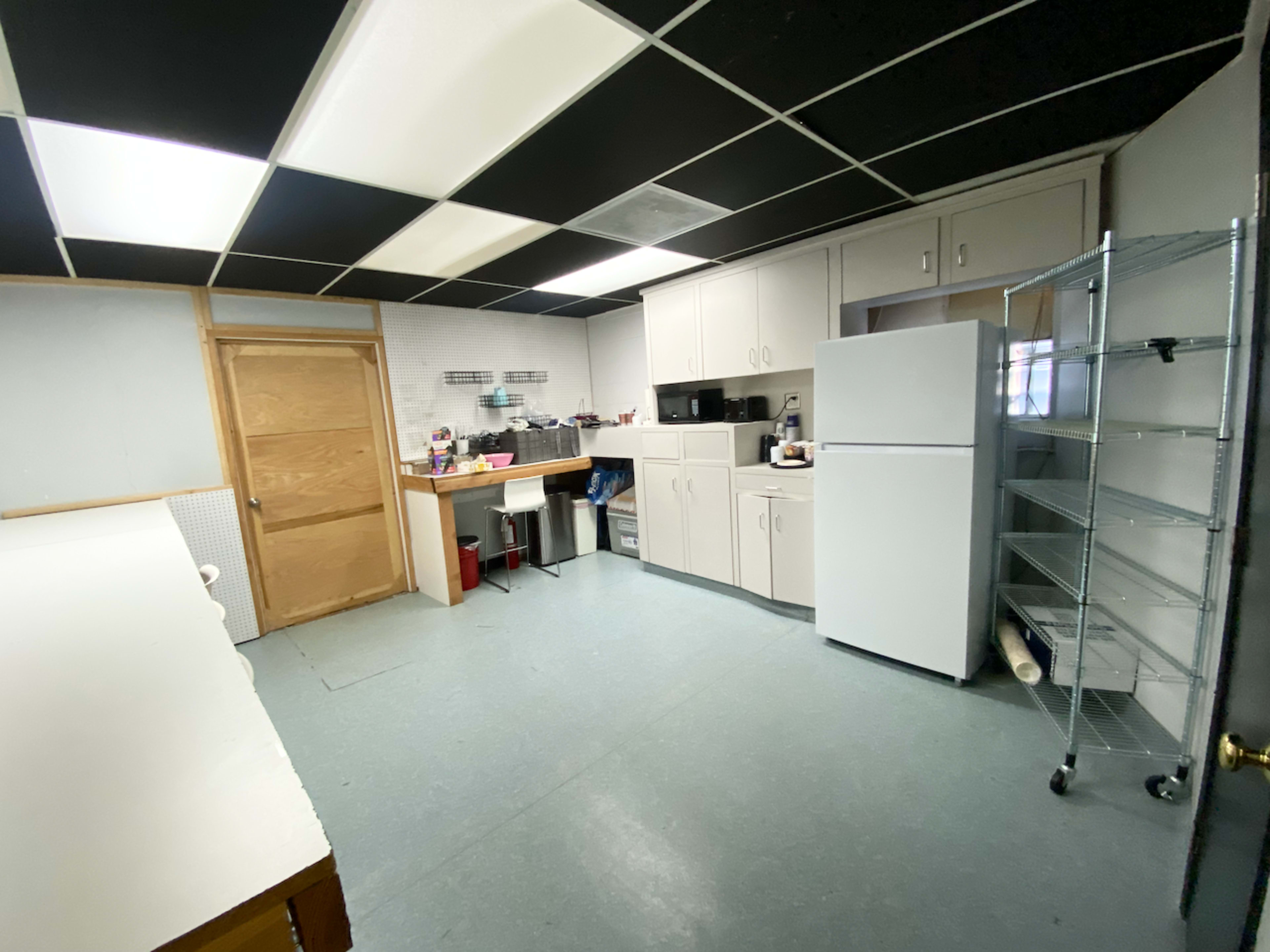 The image shows a kitchen with a gray and black tiled ceiling, white cabinets, a refrigerator, and a countertop with a seating area.
