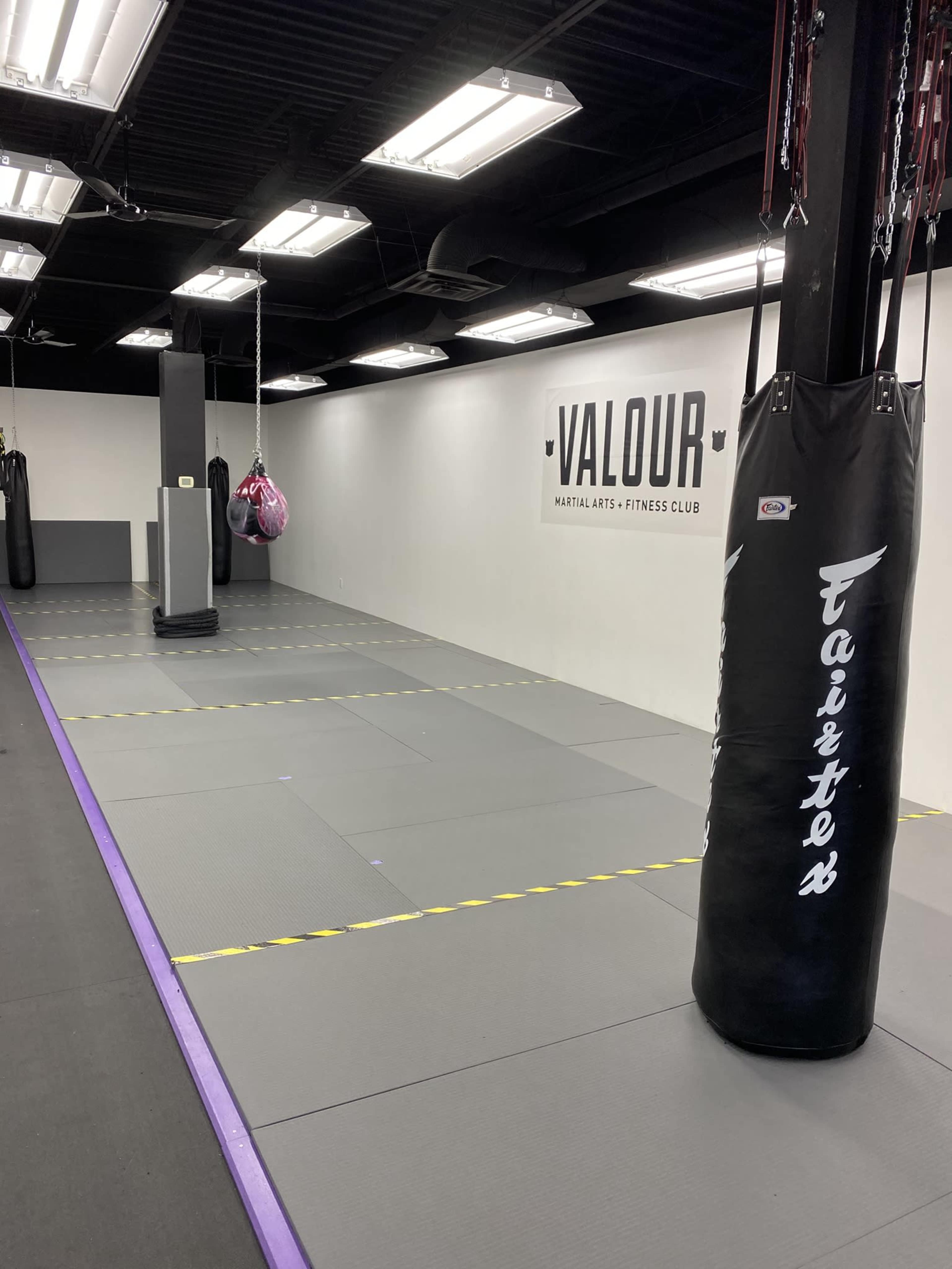An empty martial arts gym with padded flooring, a punching bag, and a wall displaying the word "VALOUR."