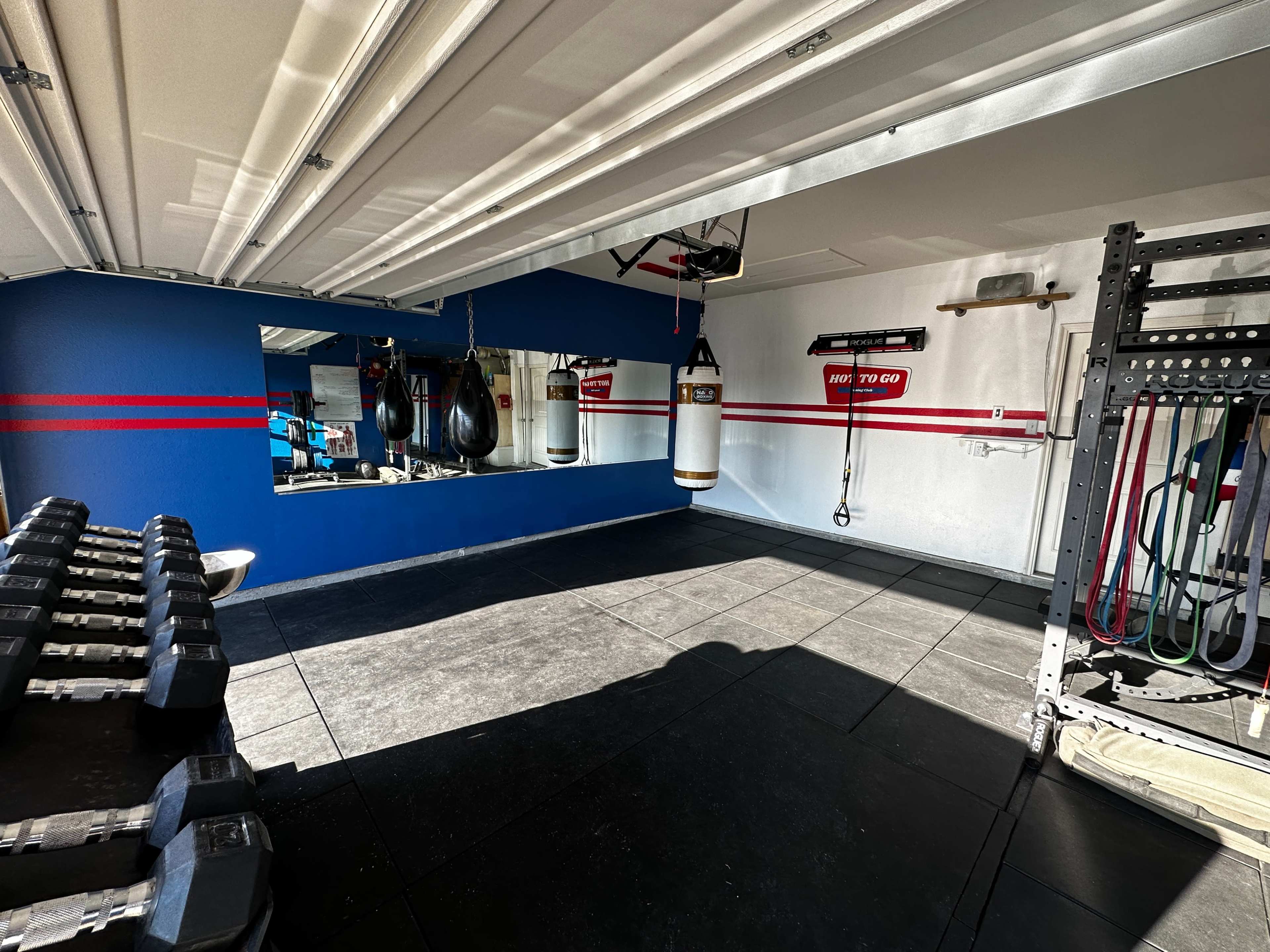 A home gym with weights, a boxing bag, and a mirror against a blue wall, featuring red stripes.