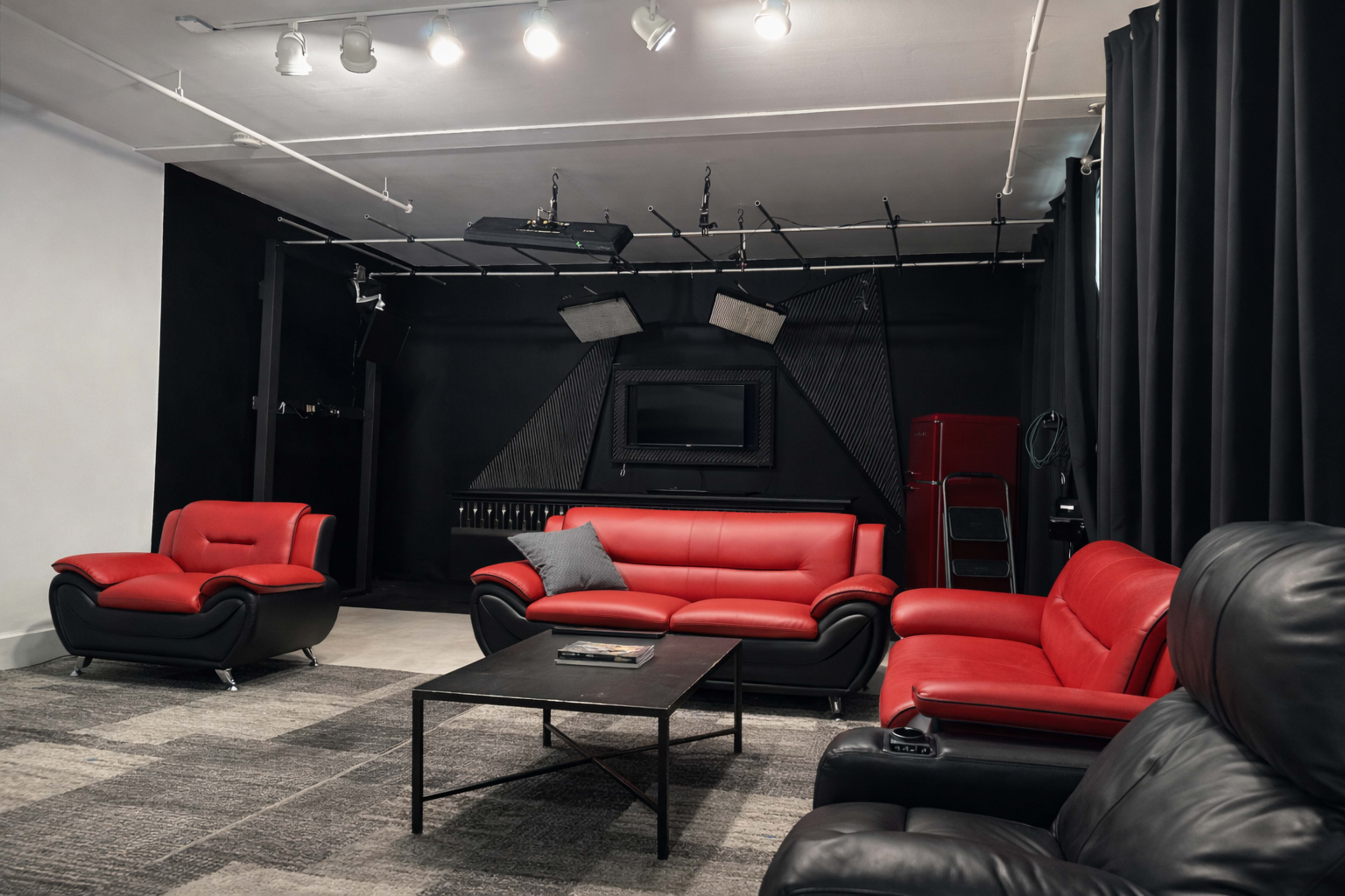 The image shows a modern lounge area with red leather sofas, a black coffee table, and dark curtains against a black wall.