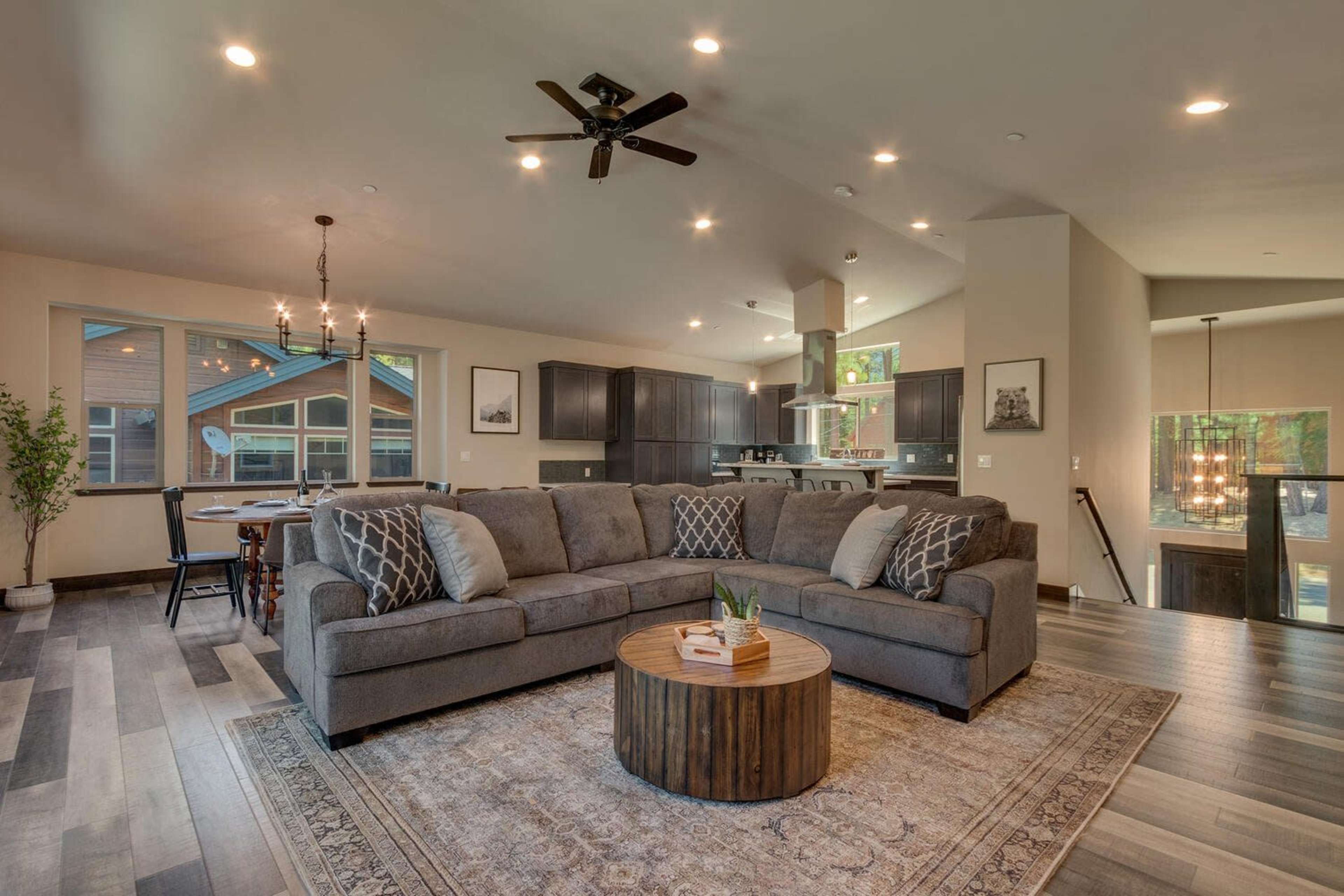 A spacious living room with a large gray sofa, a round wooden coffee table, and a view into a modern kitchen.