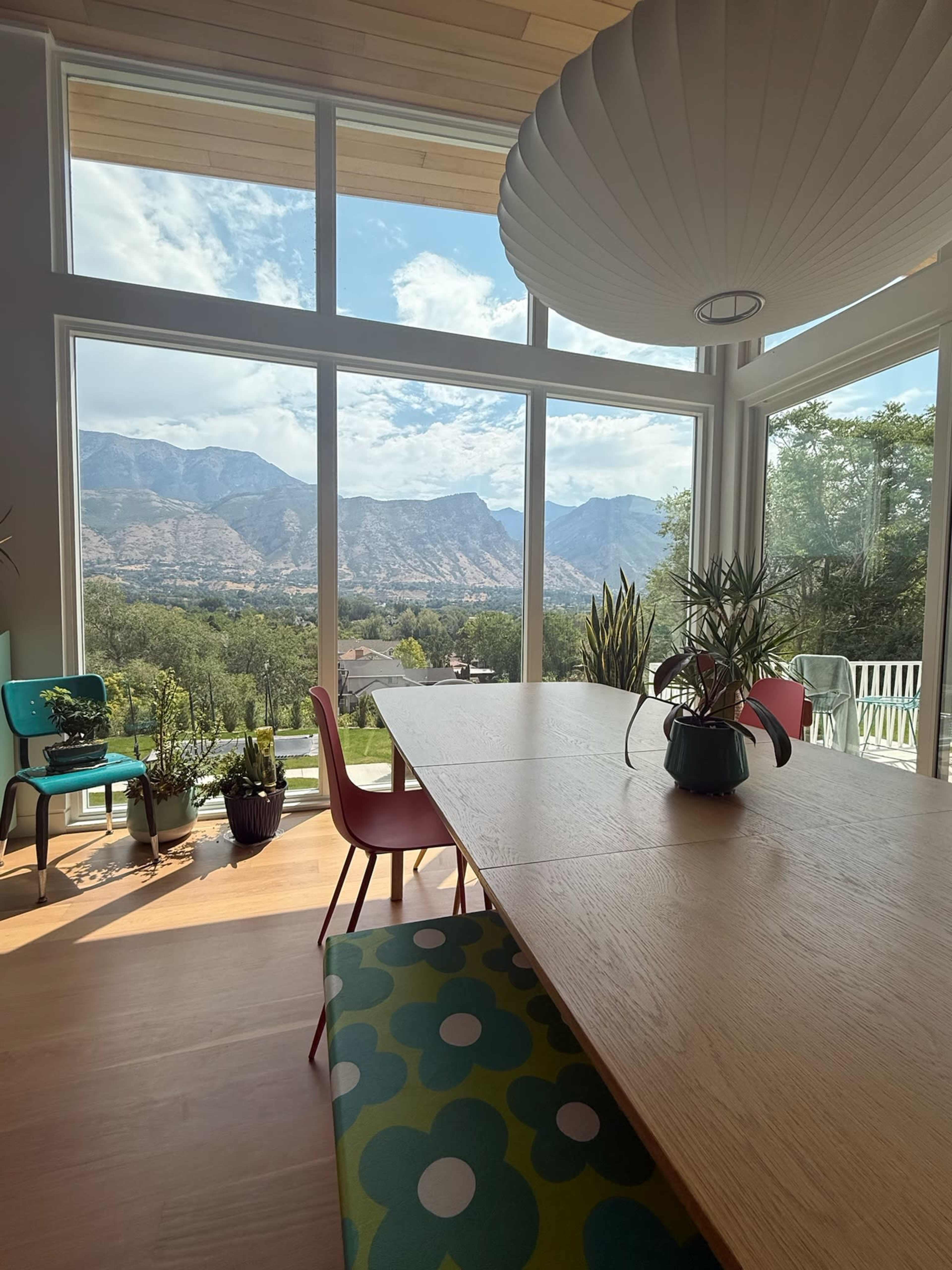 A modern dining area features a large table set against a backdrop of mountains visible through expansive windows.