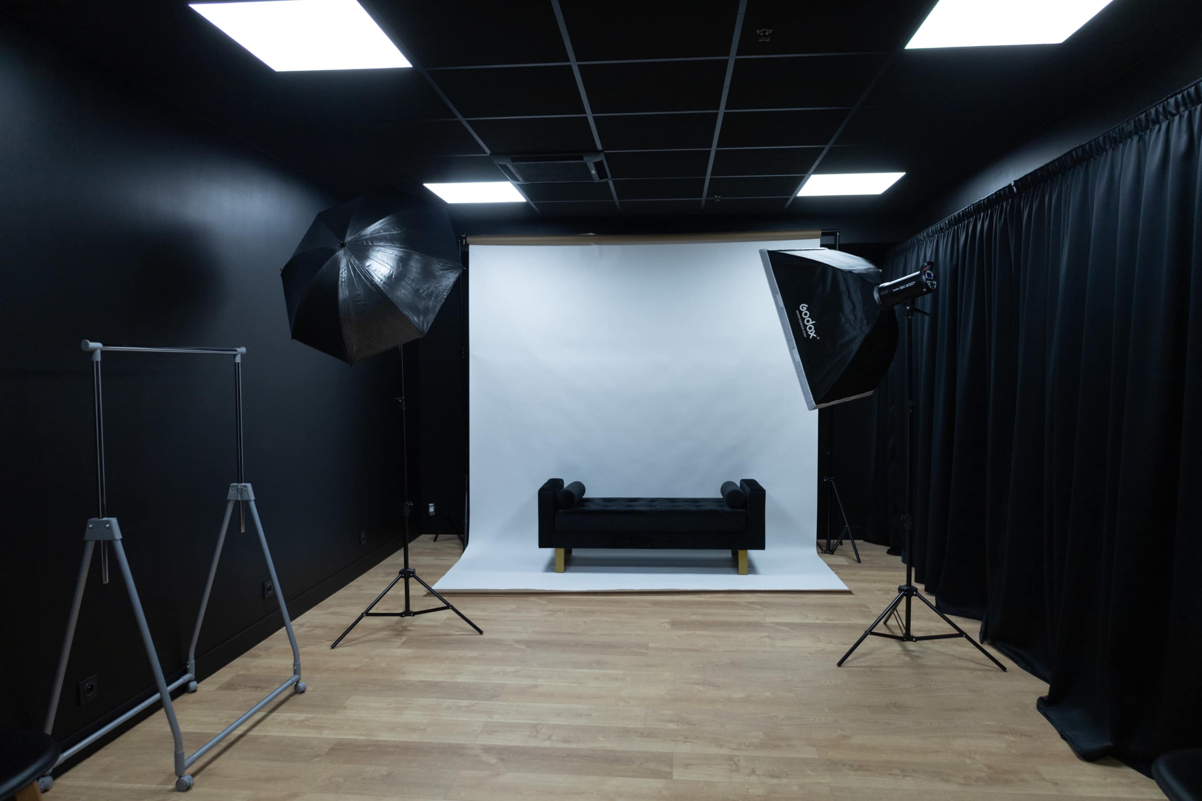A photography studio with a black backdrop, a white backdrop, a black couch, lighting equipment, and a clothing rack.