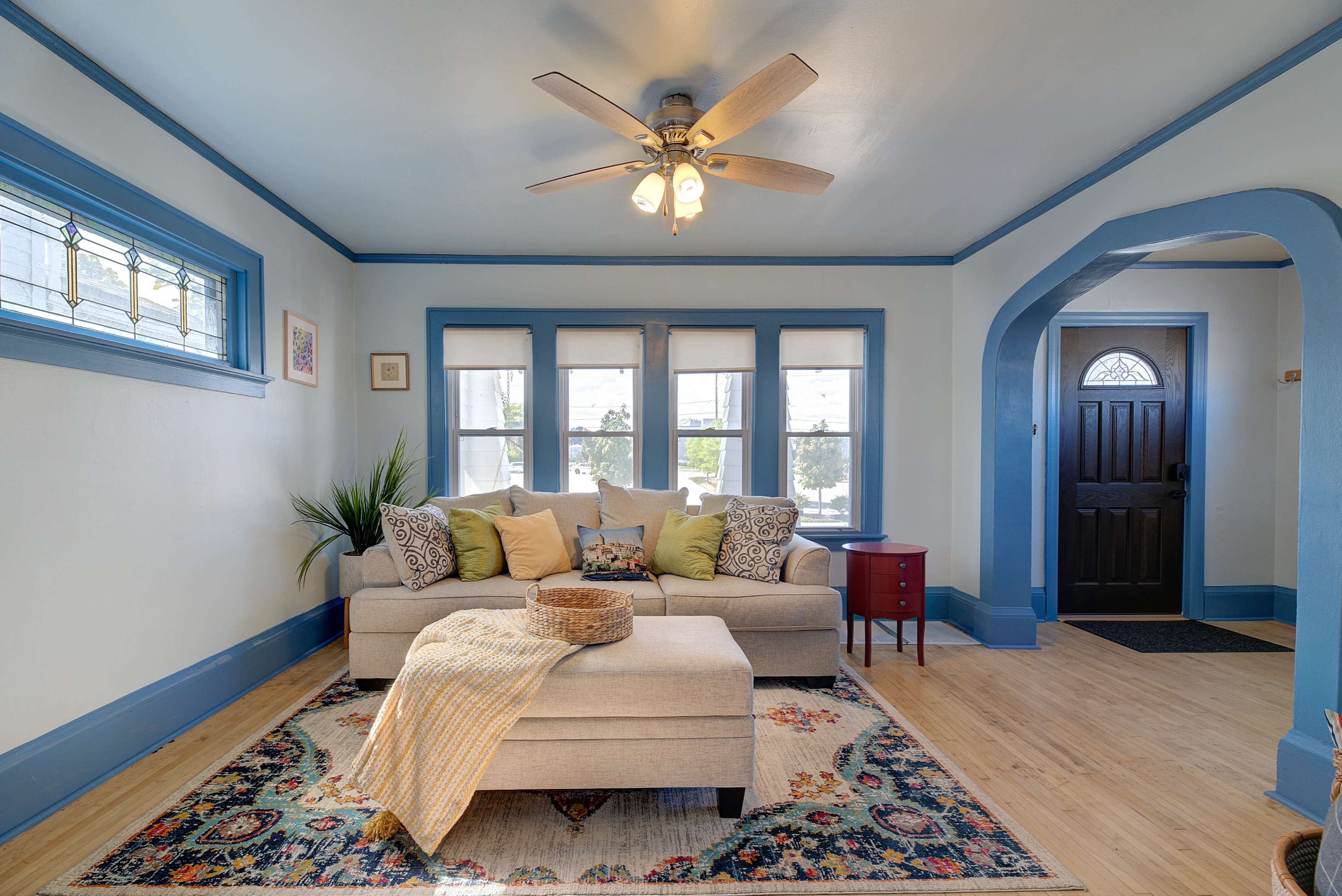 A brightly lit living room featuring a gray sofa adorned with decorative pillows, a coffee table, and an entrance with a black door.