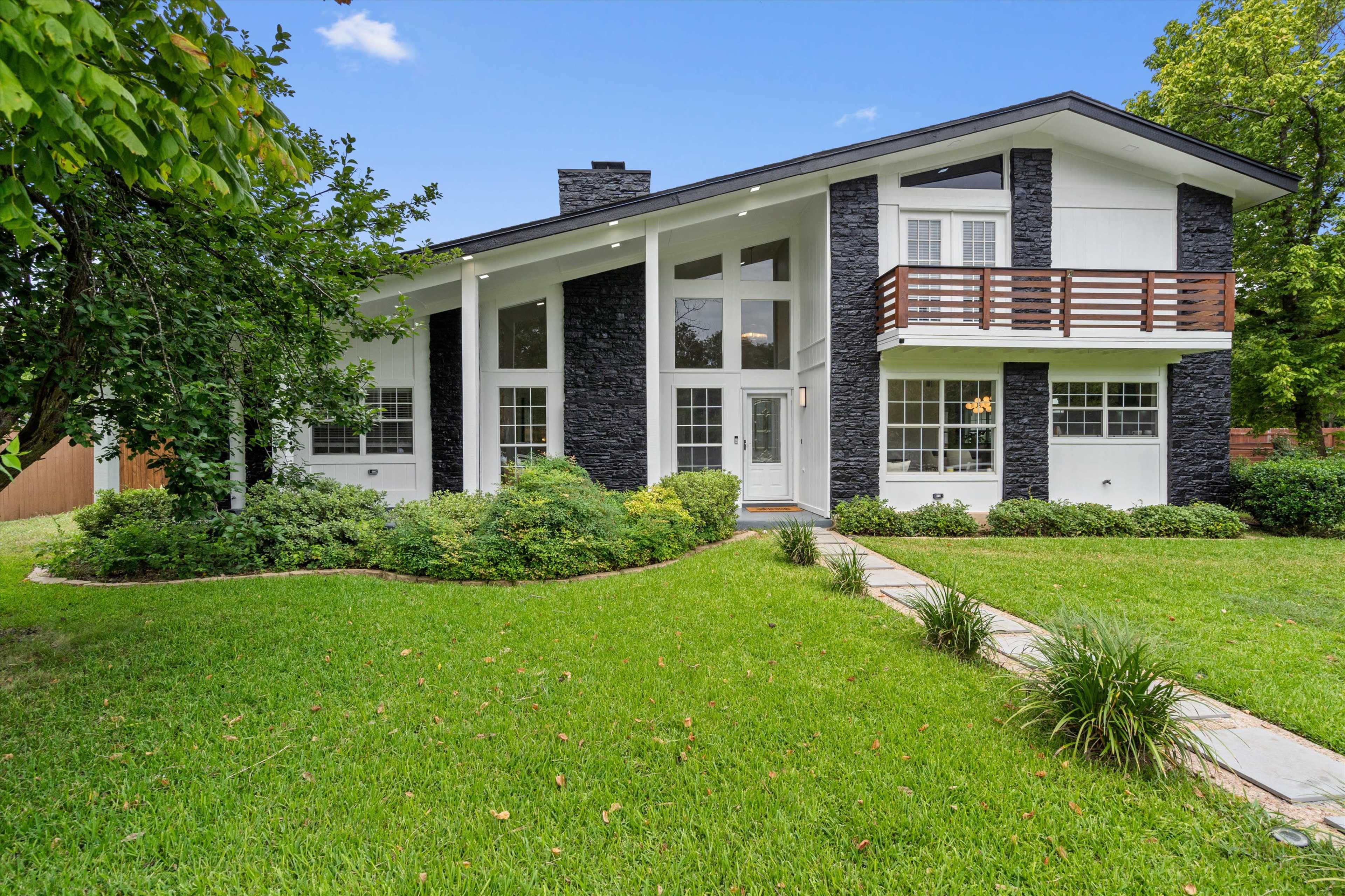The image shows a modern home with a black stone exterior and a large front yard featuring lush green grass and landscaping.