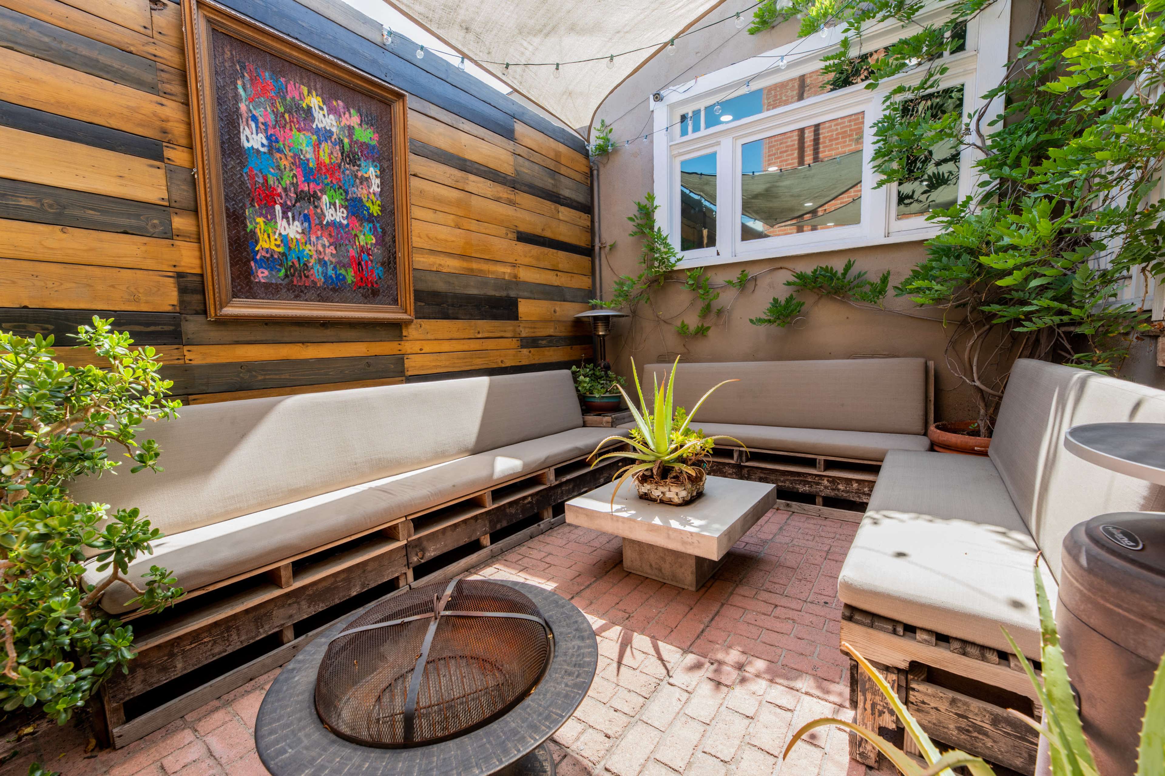 A cozy outdoor seating area with wooden walls, a rectangular coffee table, and a decorative wall art piece amidst potted plants.