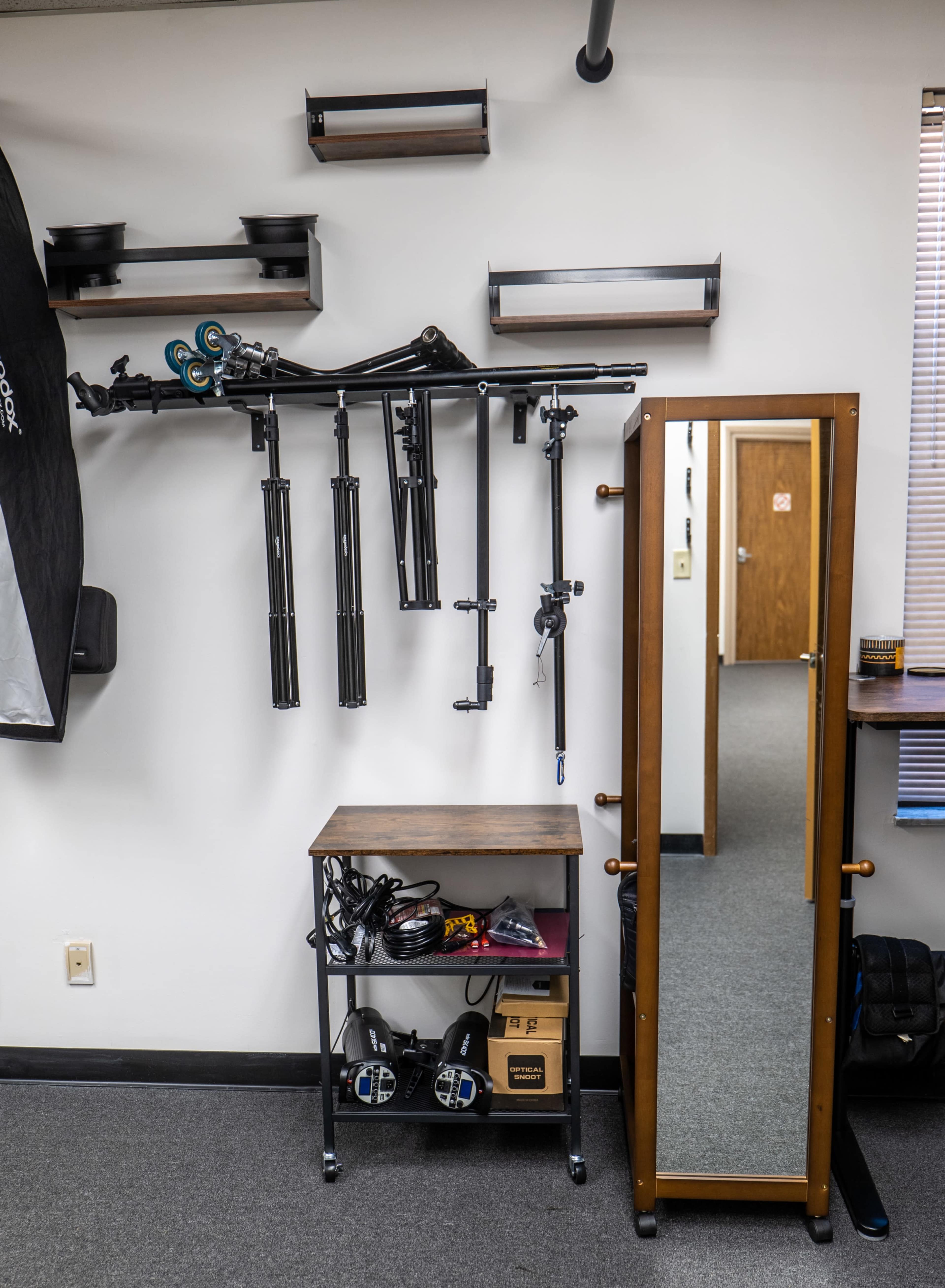 A wall-mounted setup of photography equipment alongside a tall mirror and a rolling cart with cables and audio gear.