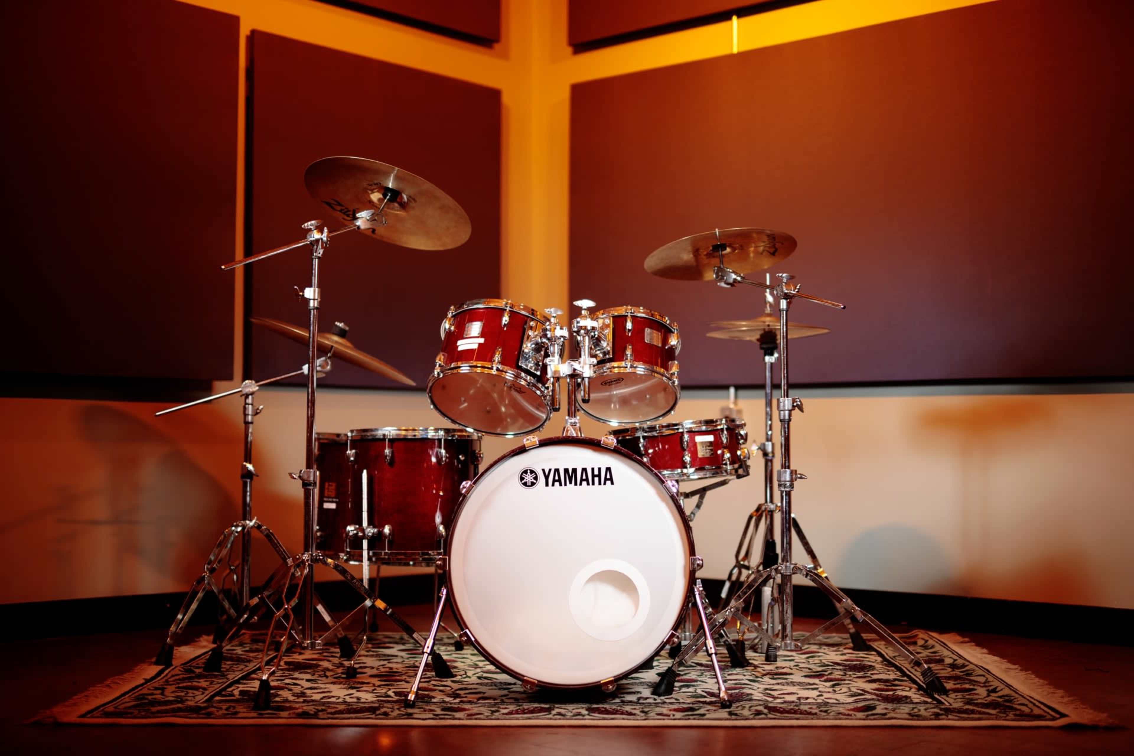 A Yamaha drum set is positioned in a soundproof studio with a patterned rug on the floor.